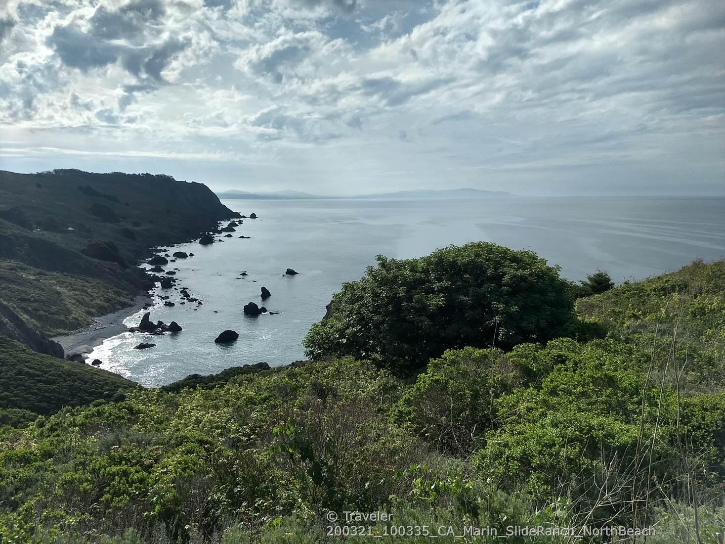 Rocky cove and green hills under a soft, cloudy sky.
