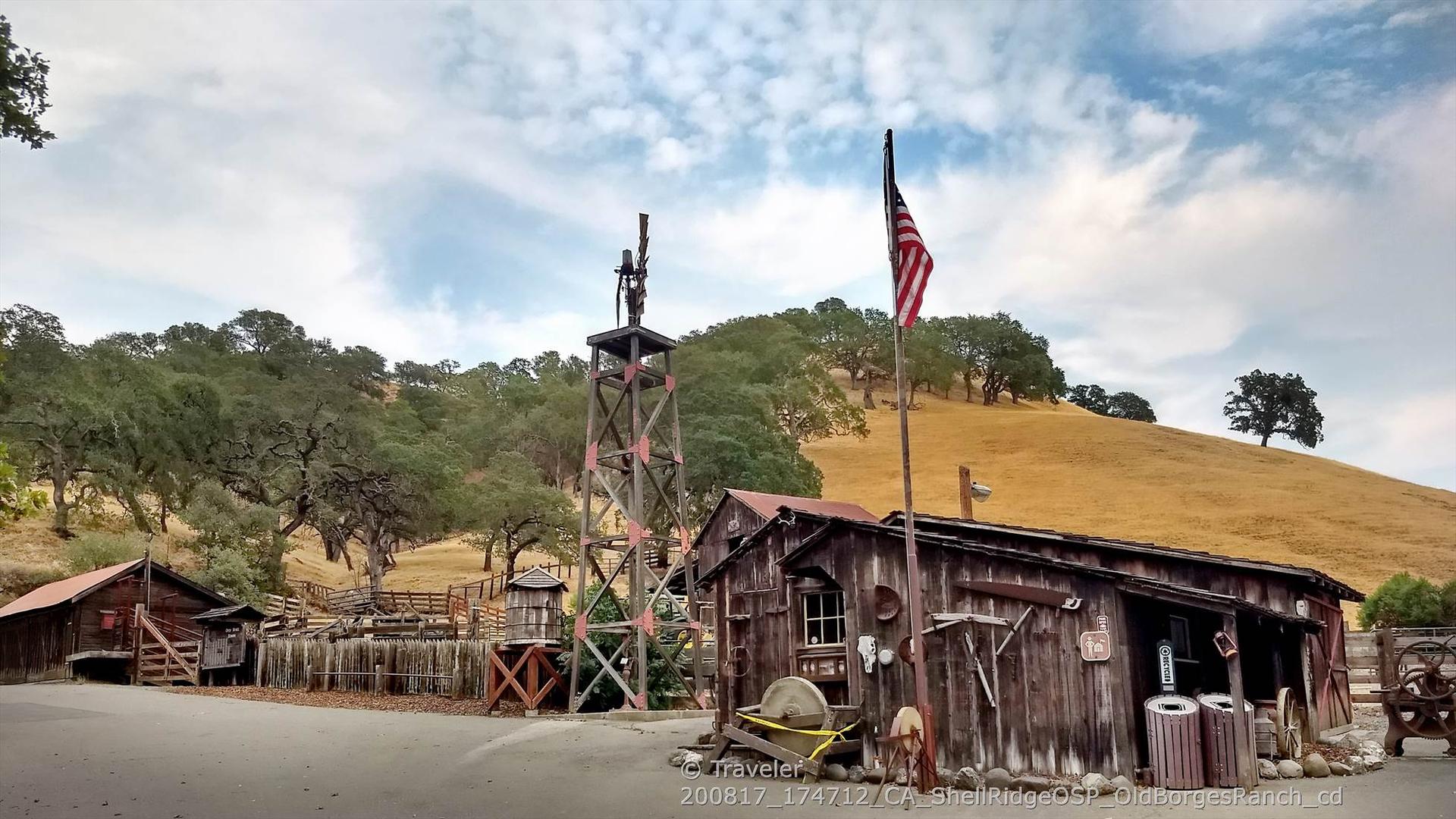 Old wooden buildings, water tower, and flag under a cloudy sky.
