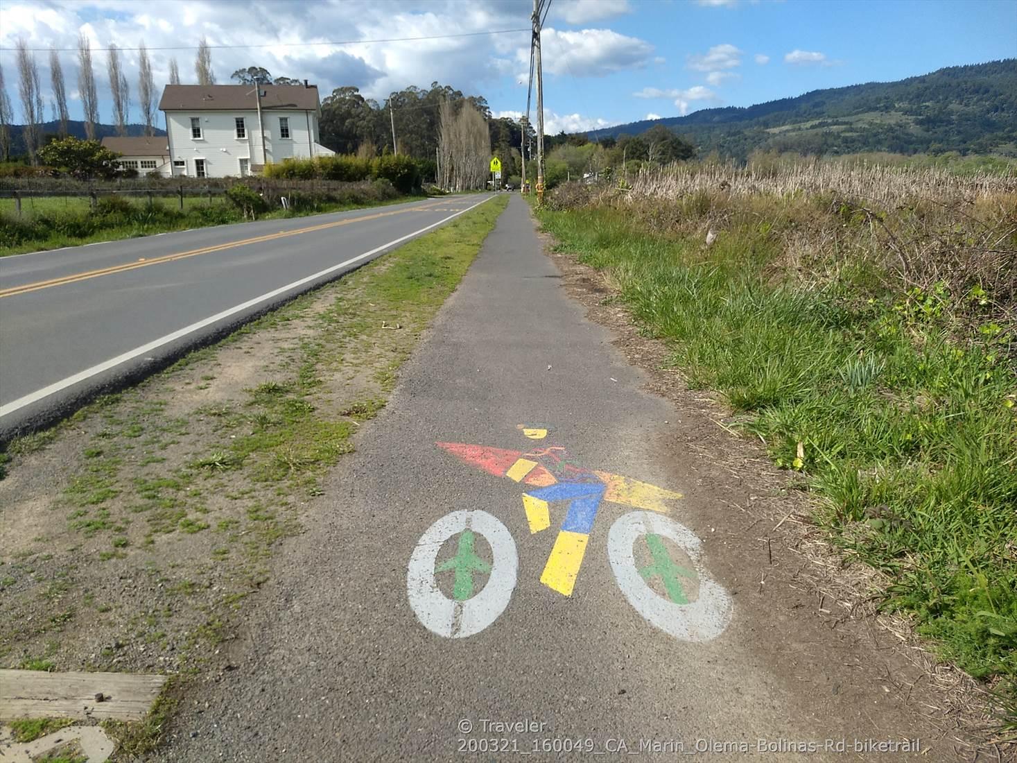 Colorful bicycle symbol painted on a paved path next to a road.