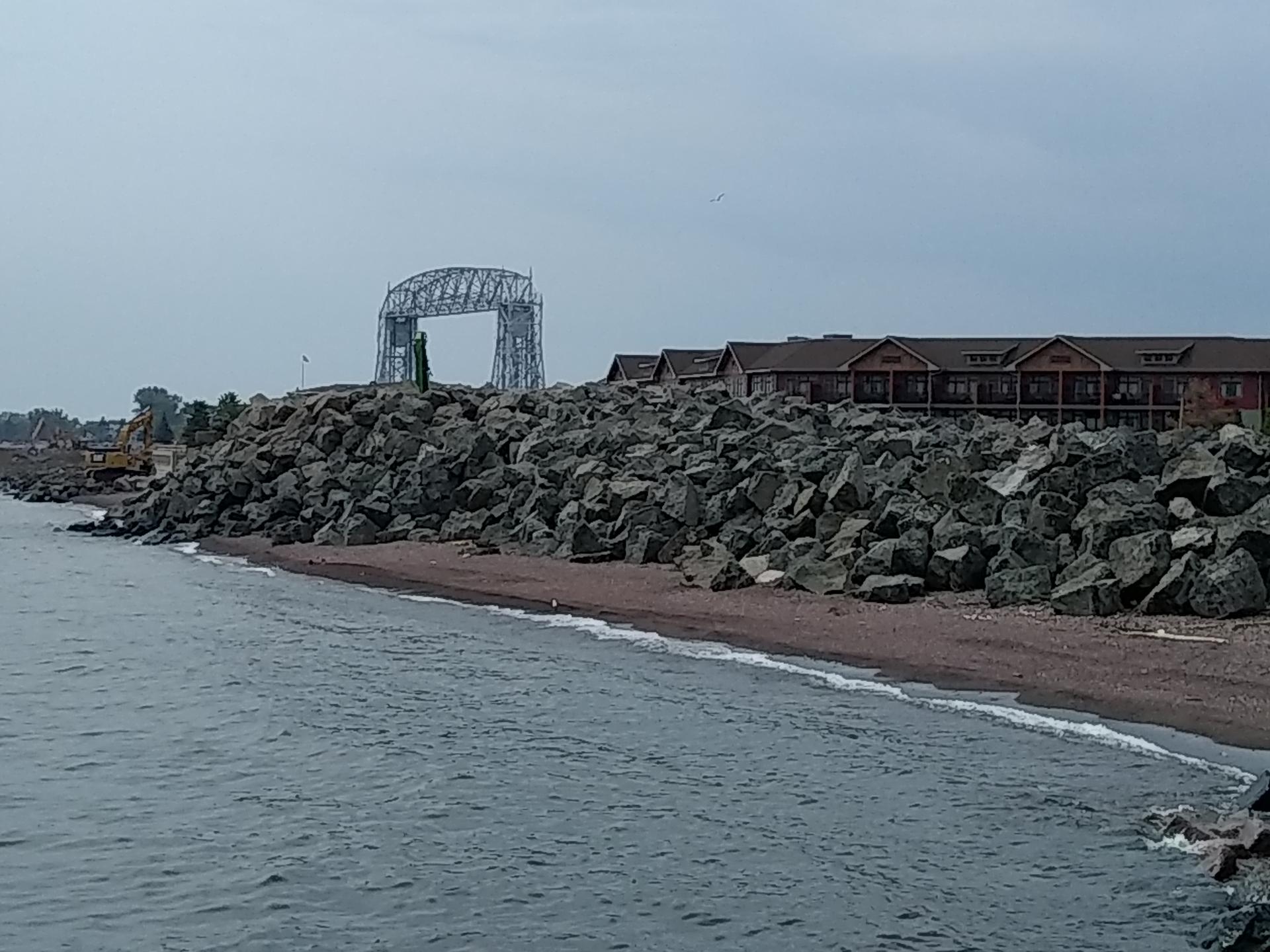 Overcast view of a rocky shoreline, buildings, and a distant bridge structure.