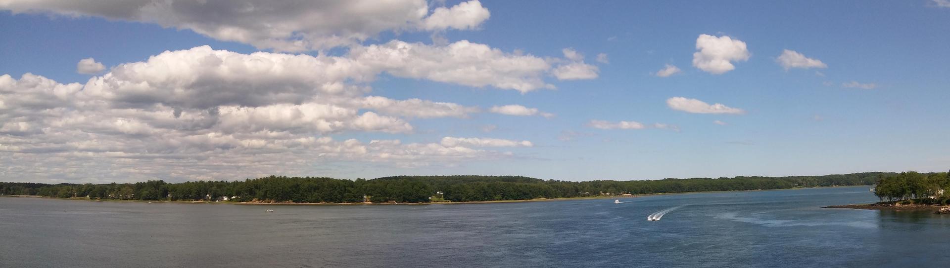 Panoramic view of a wide river with tree-lined shores under a sunny sky.