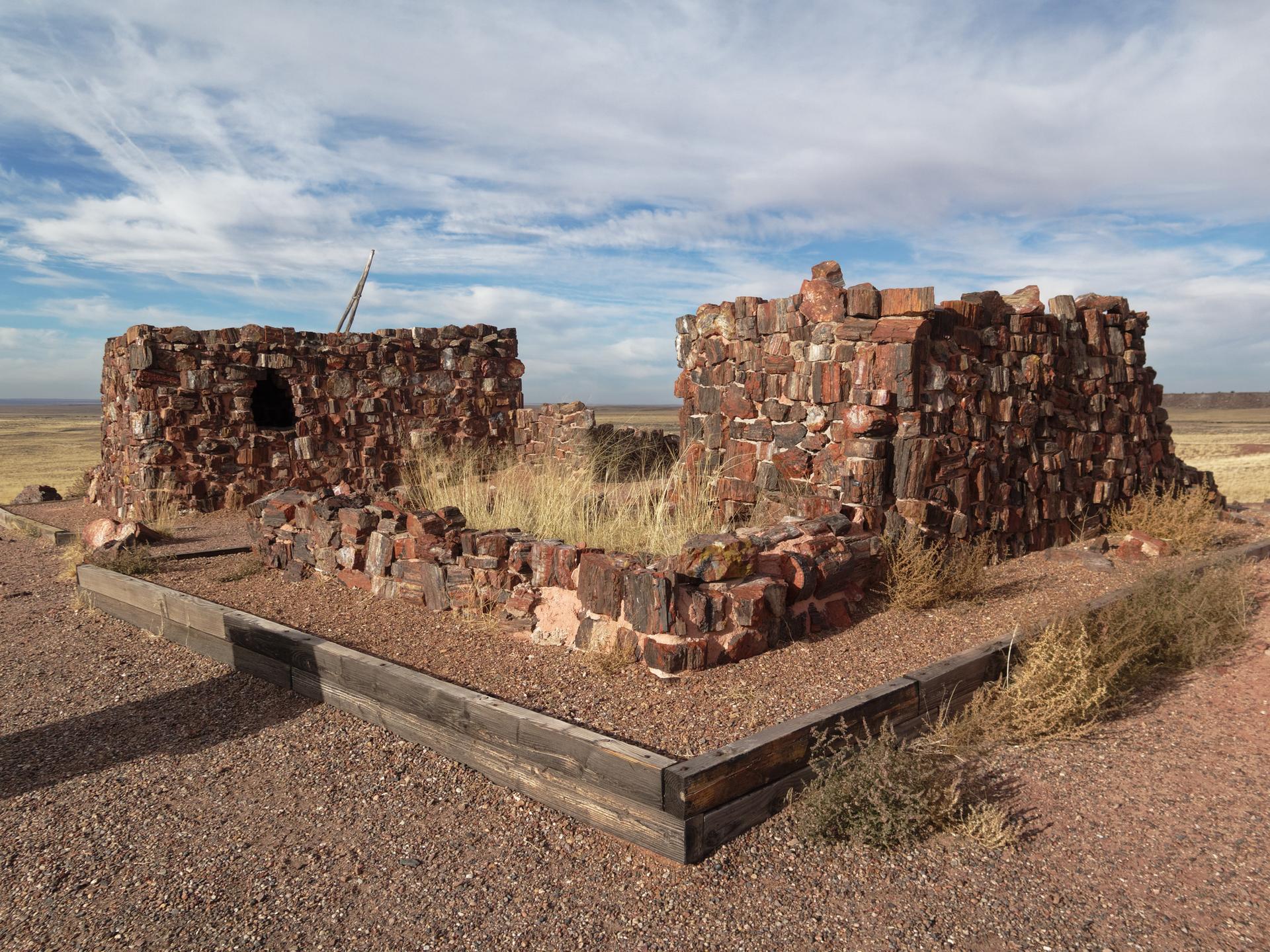Ancient stone ruins with dry grass inside, under a partly cloudy sky.