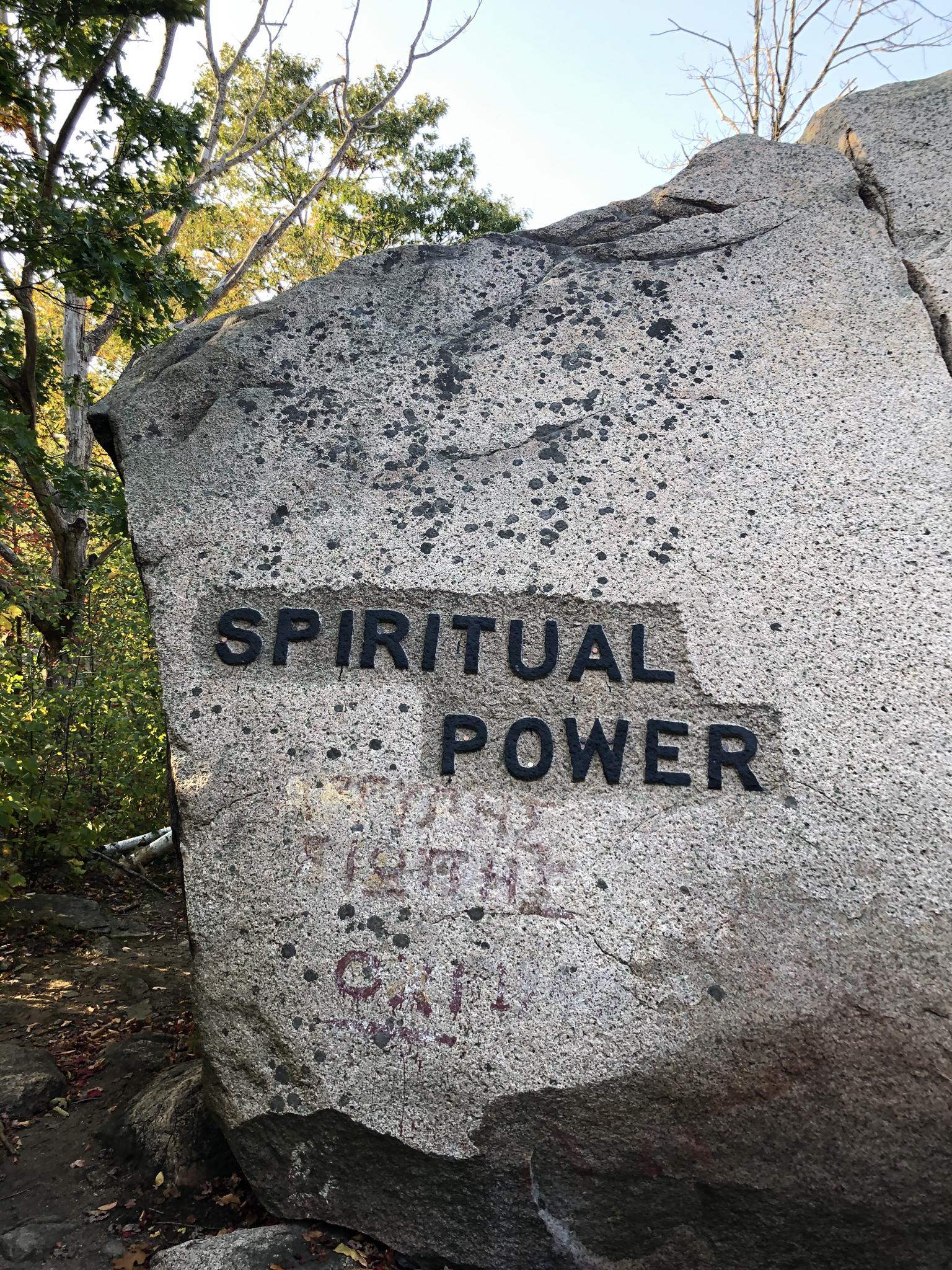 Large gray boulder with "SPIRITUAL POWER" carved, under bright natural light.