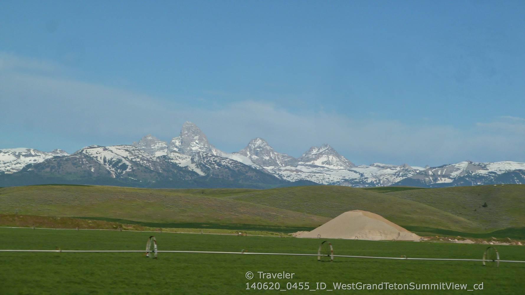 Distant snow-capped mountains rise above green rolling fields under a clear blue sky.