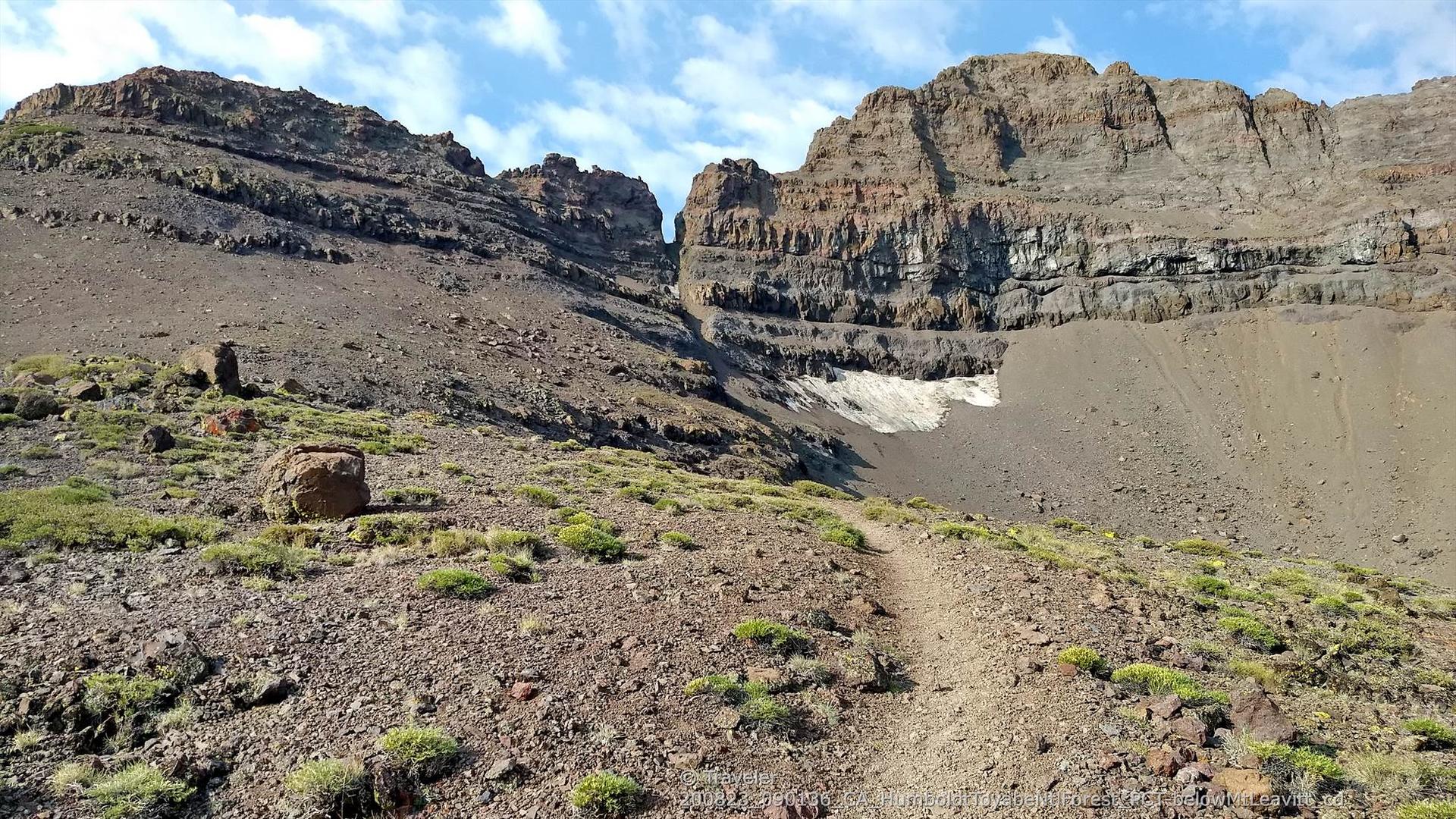 A dirt trail leads towards a dramatic mountain pass with steep rock walls.