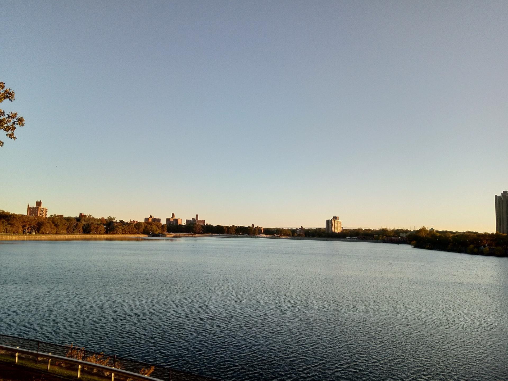 Wide view of a large lake with distant buildings under a clear golden sky.