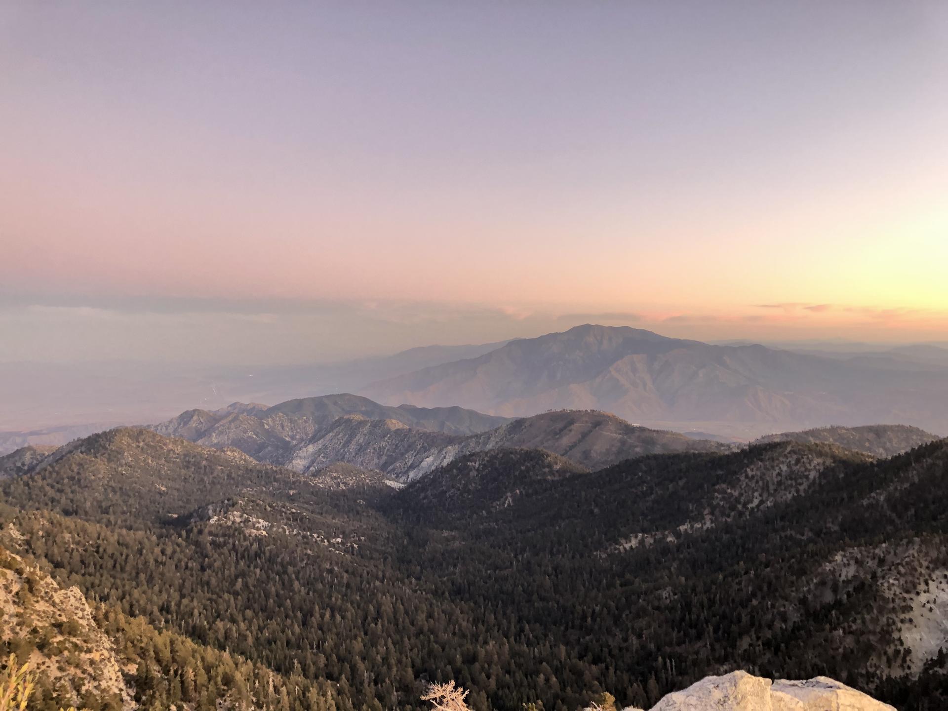 Mountain range at sunset, with soft pink and purple hues in the sky.