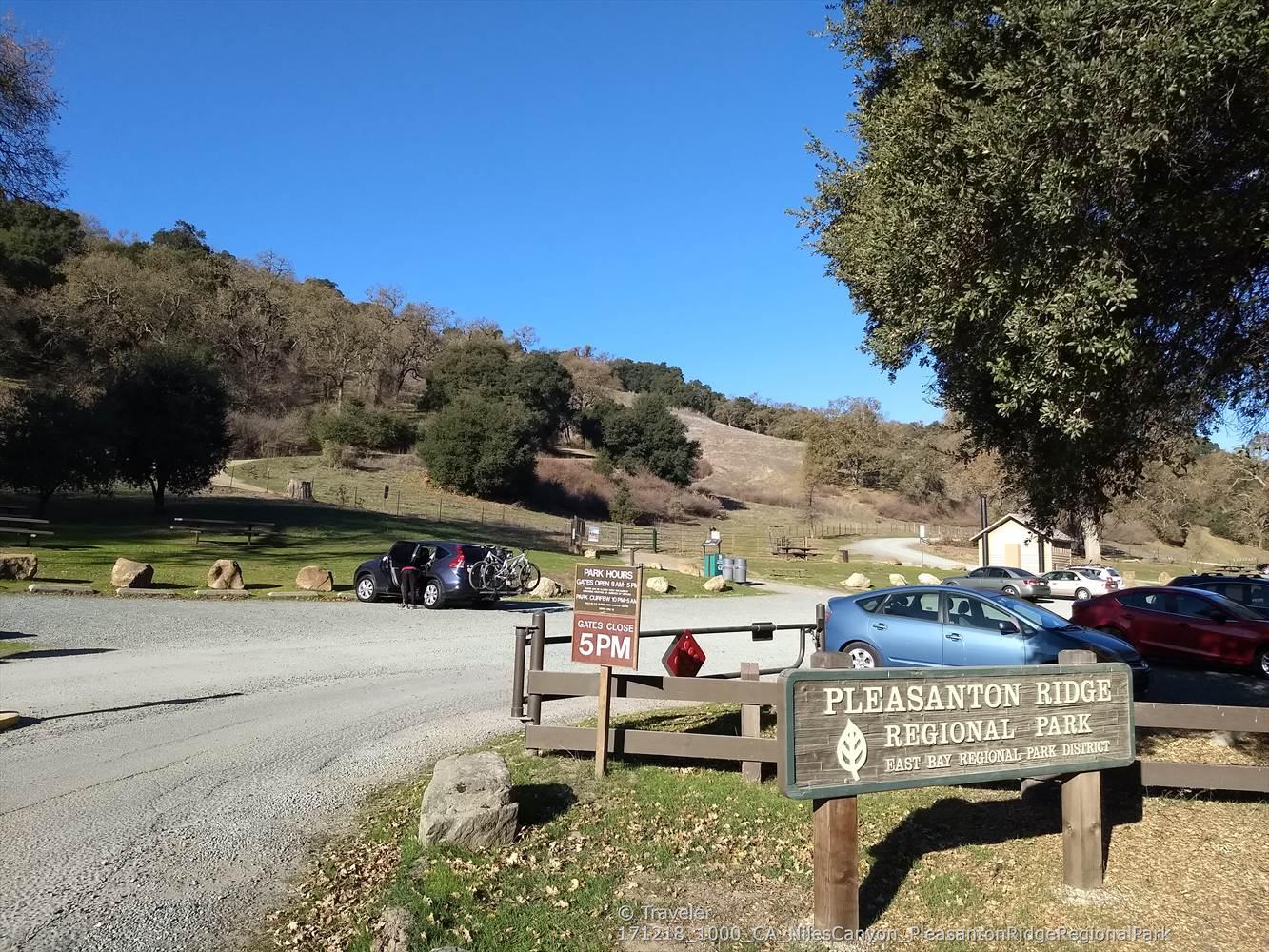 A sunny parking area with cars, a wooden sign, and dry hills.