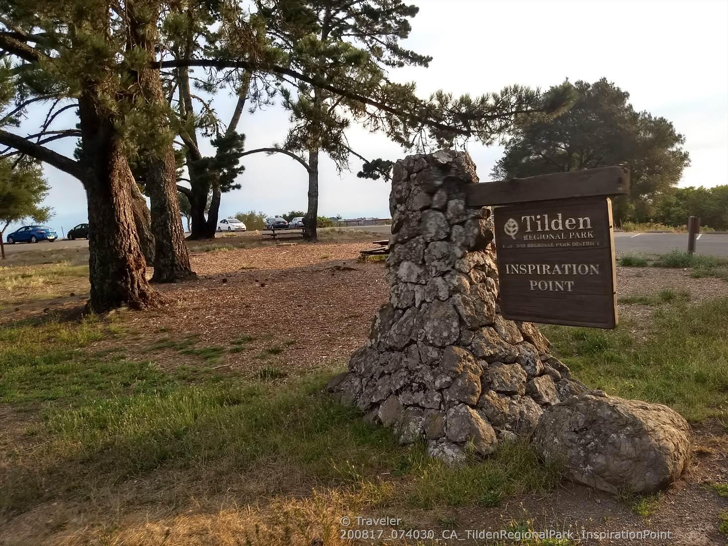 Stone monument with a wooden sign in a grassy area with tall trees.