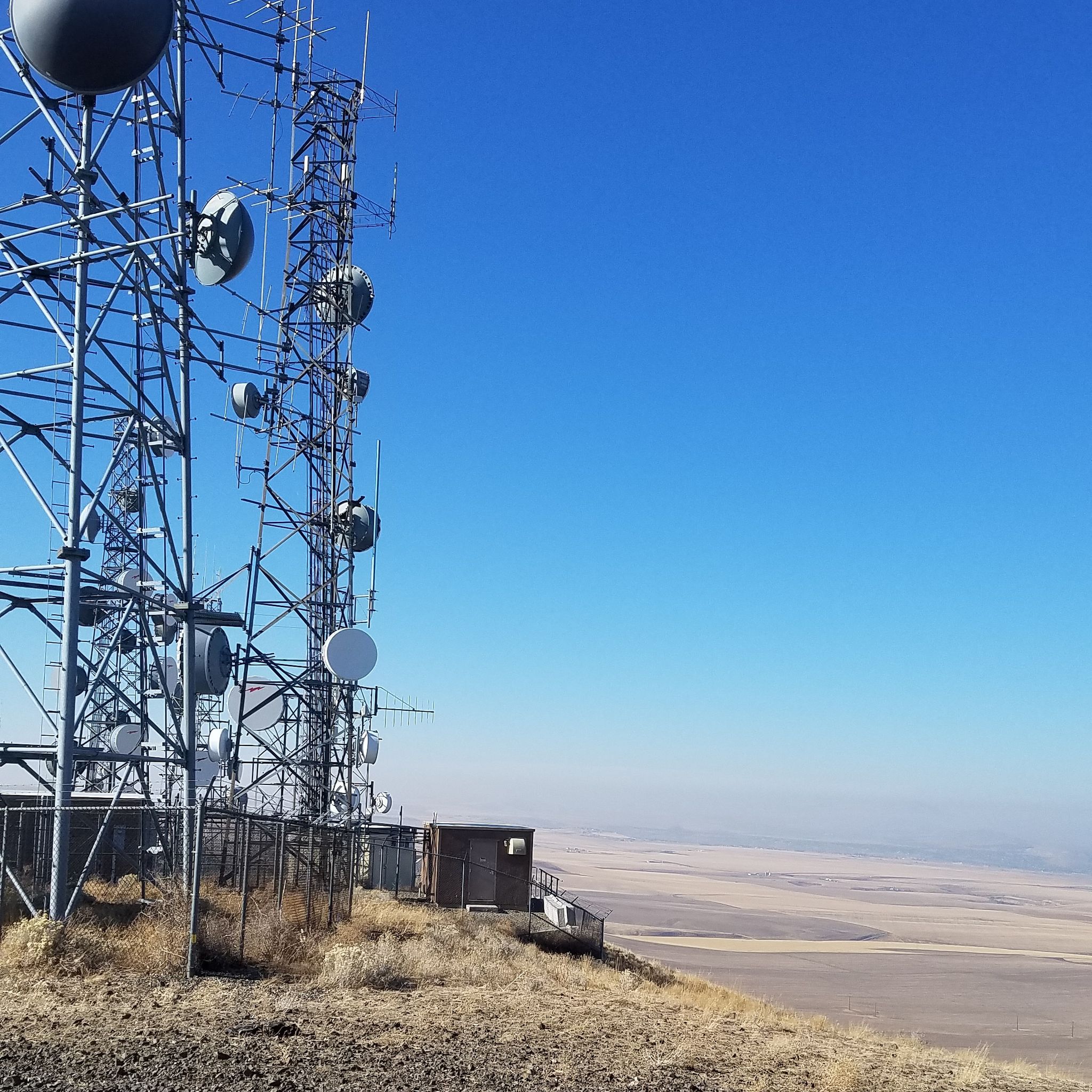 Communication towers on a dry hill overlooking a vast plain under a clear blue sky. - Jump Off Joe Trail