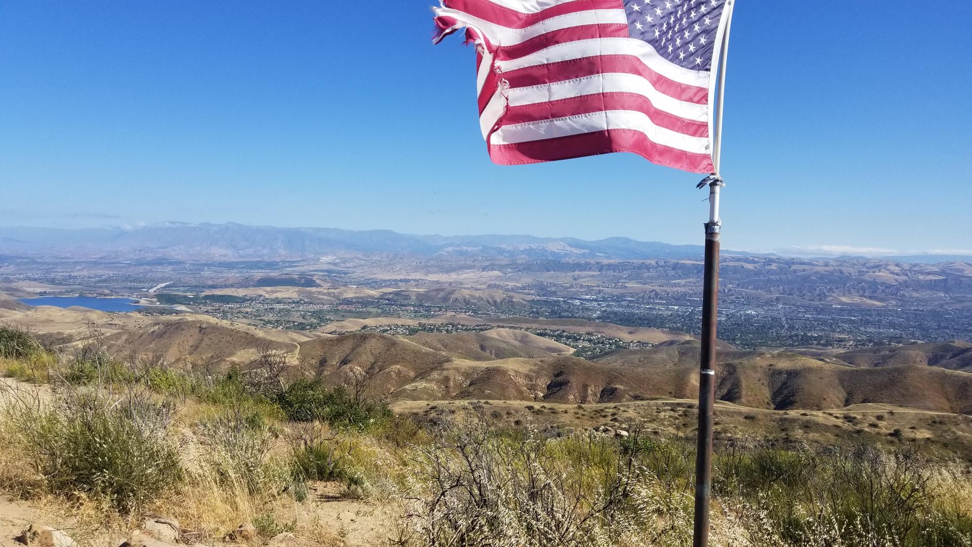 American flag flying over dry hills and a distant lake on a sunny day.