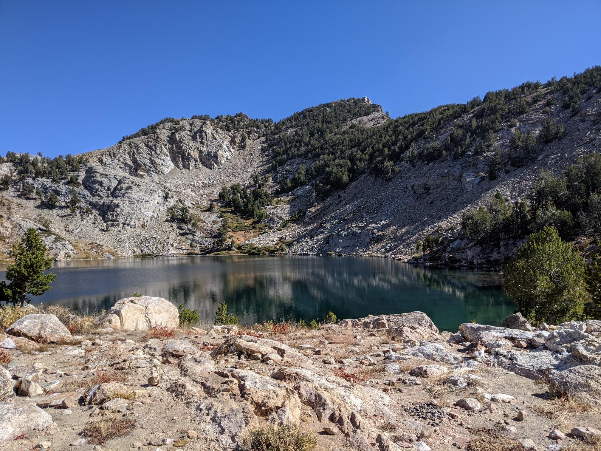 Clear mountain lake nestled among rocky slopes and green pine trees in daylight.