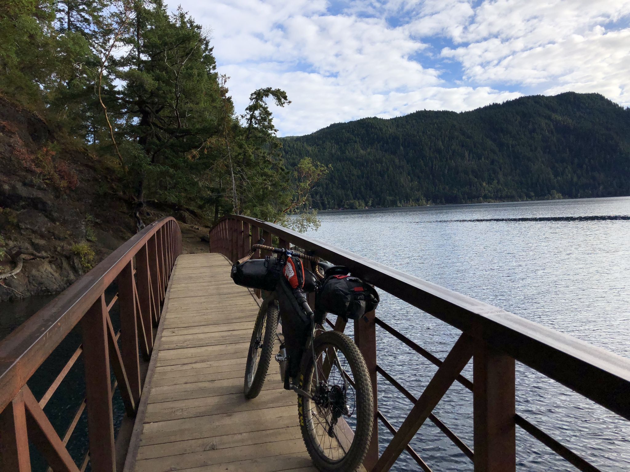 Bicycle parked on a wooden bridge overlooking a calm lake and forested hills. - Devil's Punchbowl via Spruce Railroad Trail