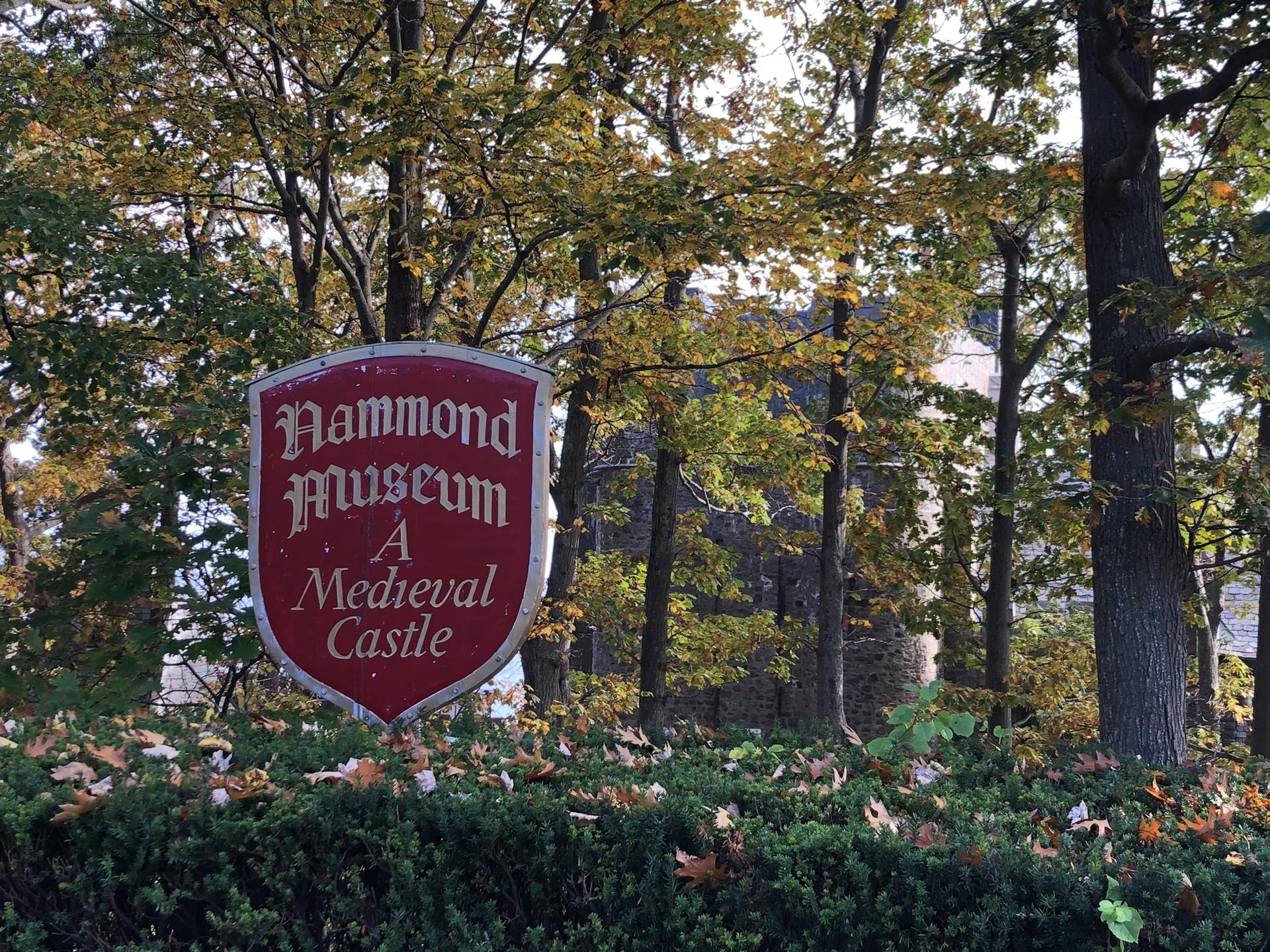 Red sign for a 'Medieval Castle' museum, partially obscured by autumn trees.
