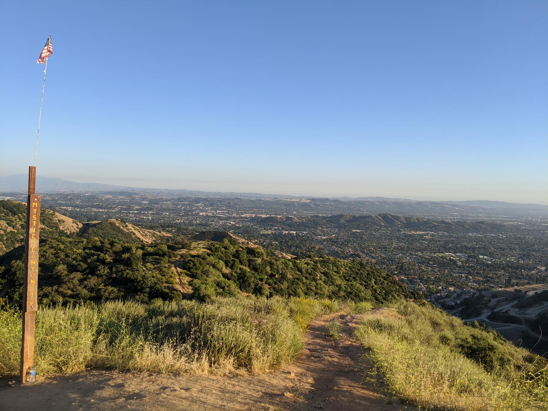 Sunny hilltop path with a small flag overlooking a vast distant city.