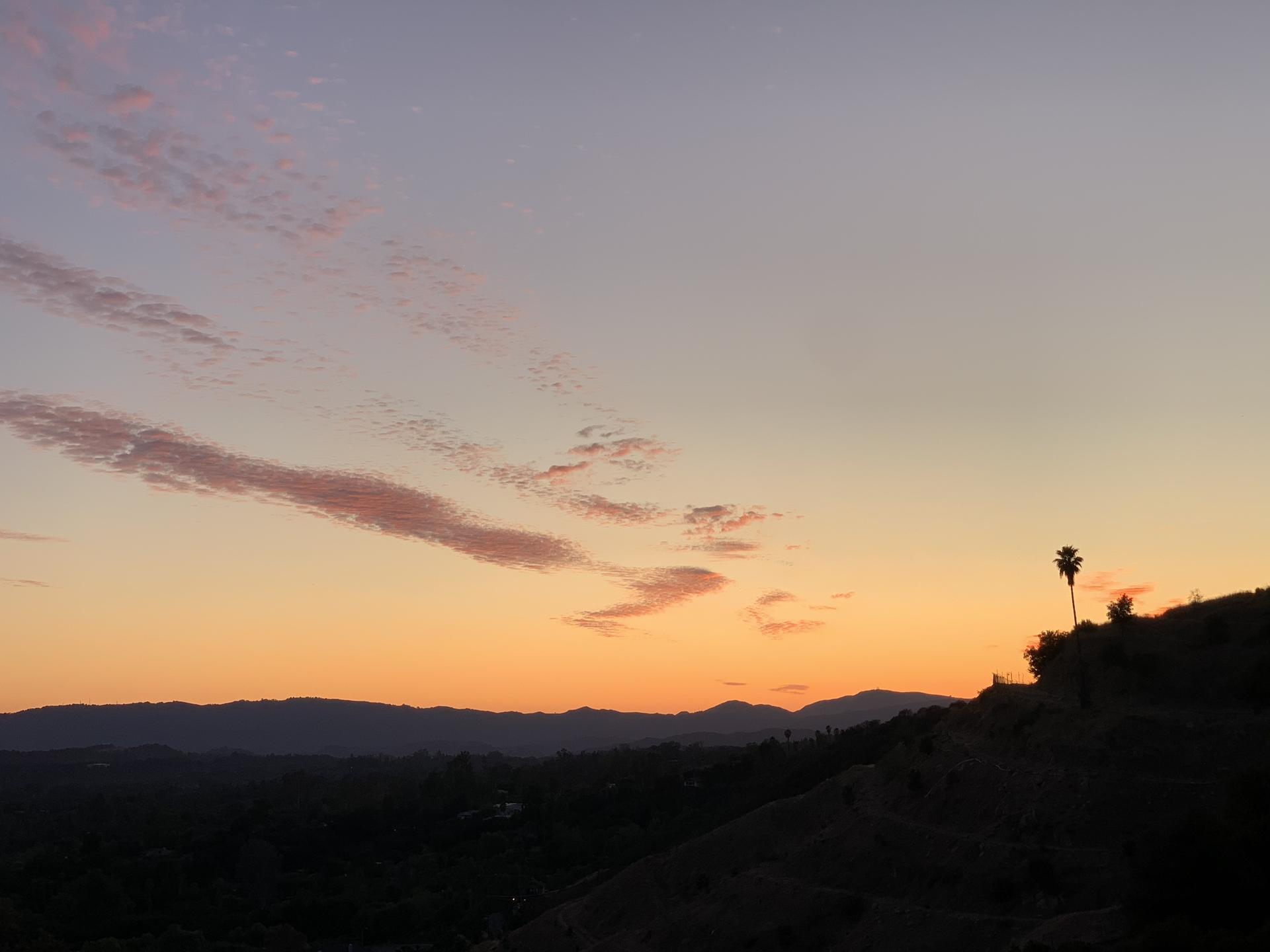 Warm sunset sky with orange and purple hues over silhouetted hills.