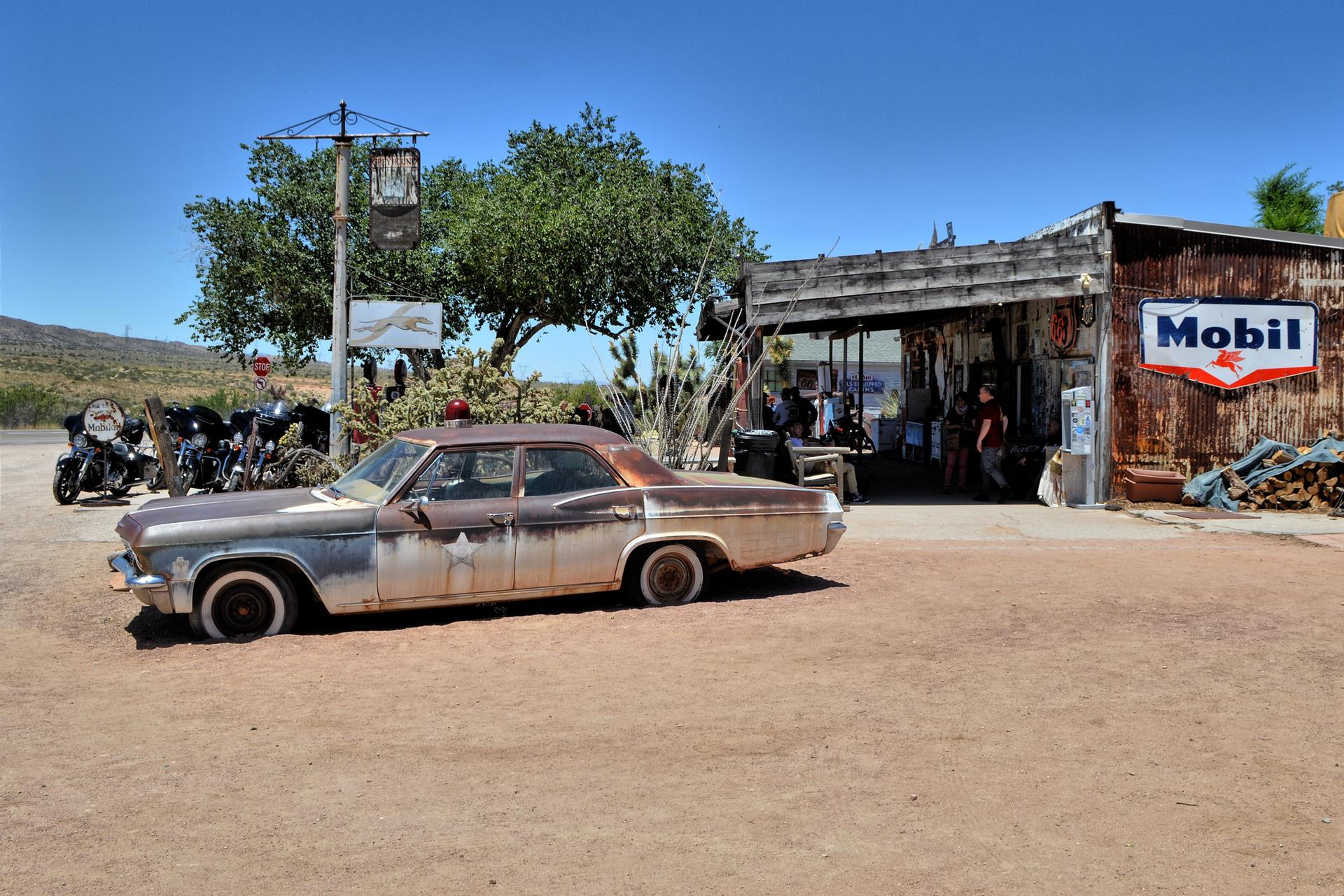 Rusty vintage car parked in front of an old building with a Mobil sign.