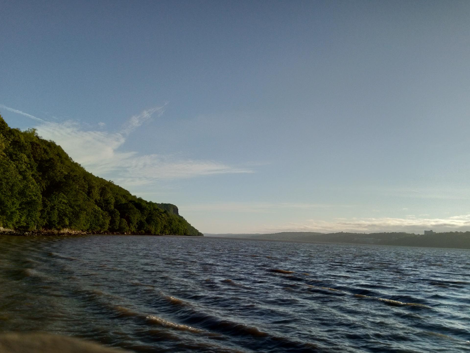 Wide view of a large body of water next to a green, forested cliff.