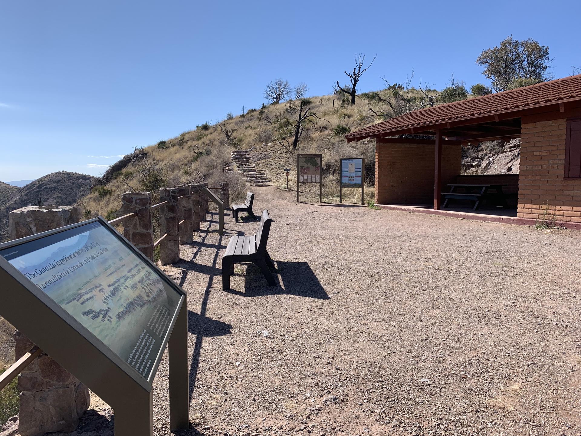 Information kiosk, benches, and building on a sunny, rocky hillside.