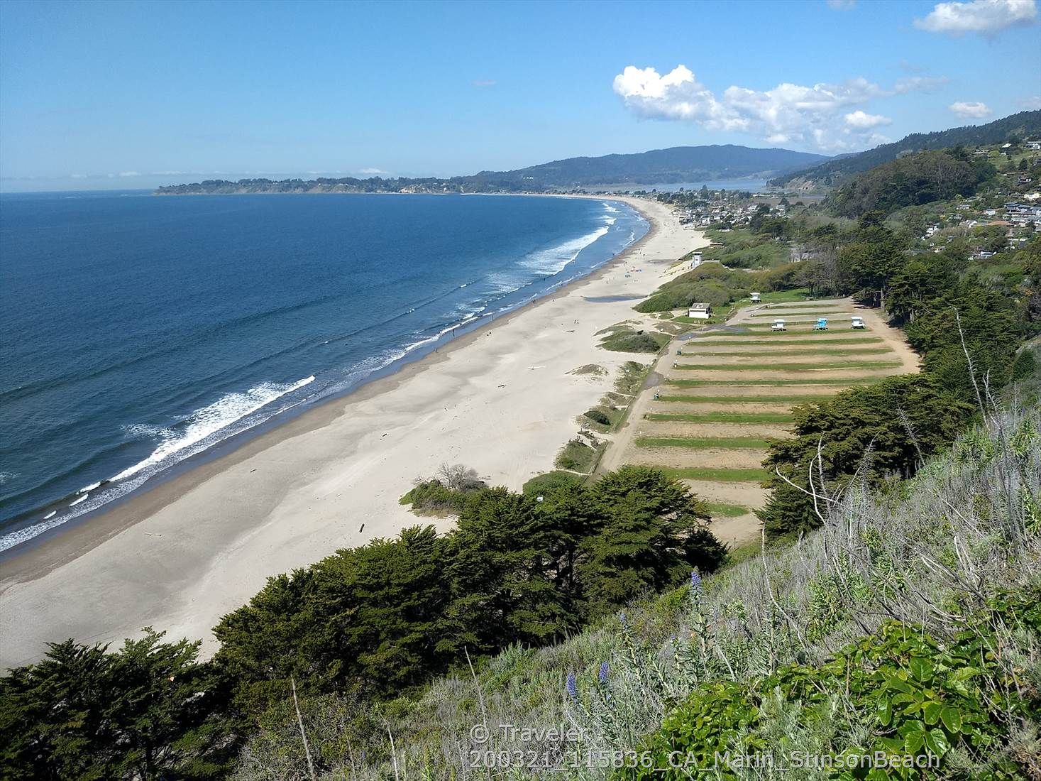 Expansive sandy beach, blue ocean, and coastal town under bright sun. - Muir Woods Loop