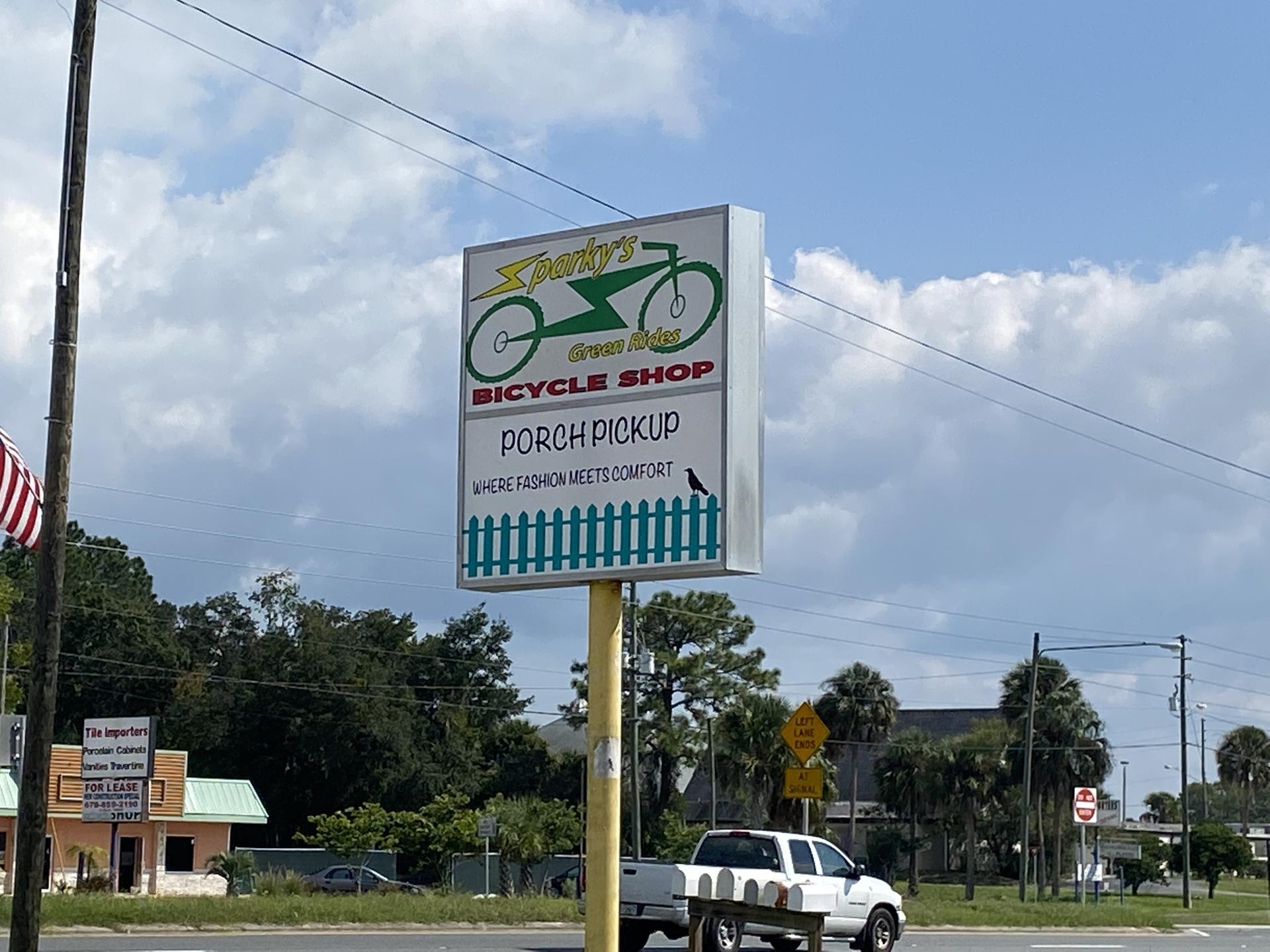 Roadside sign for Spanky's Bicycle Shop under a bright, cloudy sky.