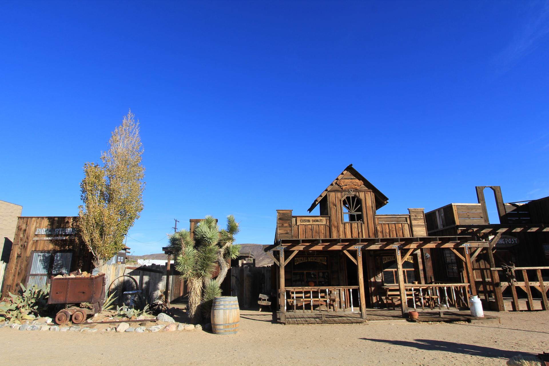 Old wooden buildings and desert plants under a clear blue sky.