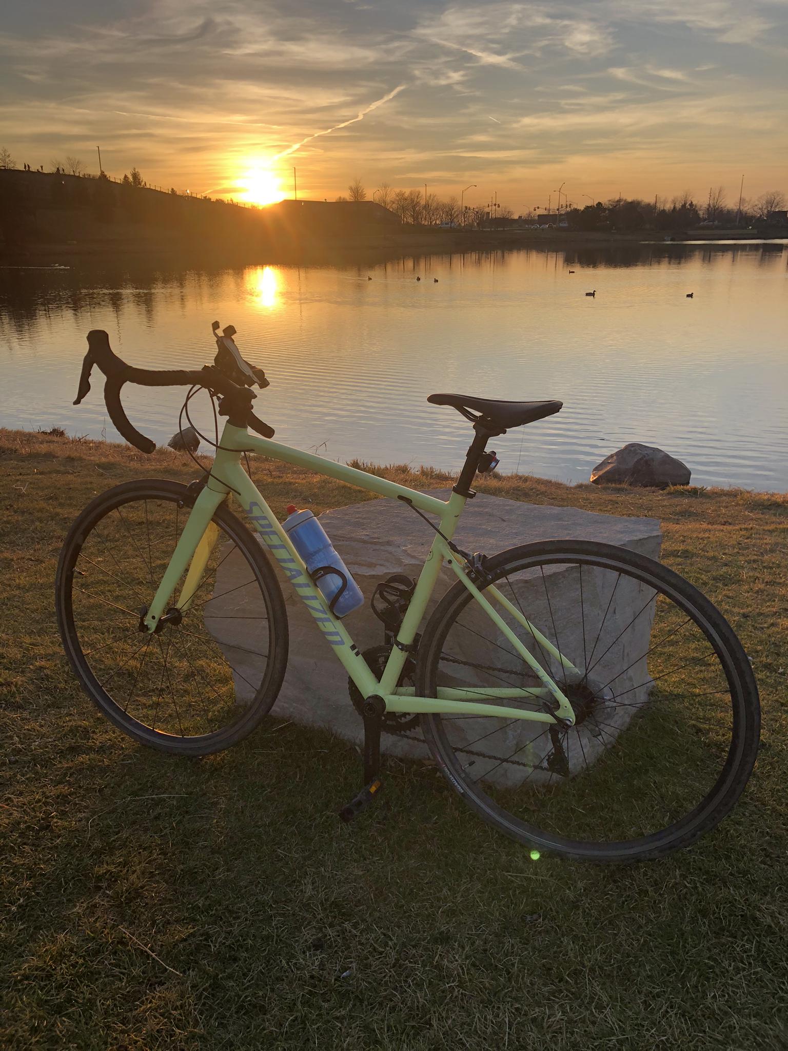 Light green bicycle rests by a calm lake at golden hour sunset.