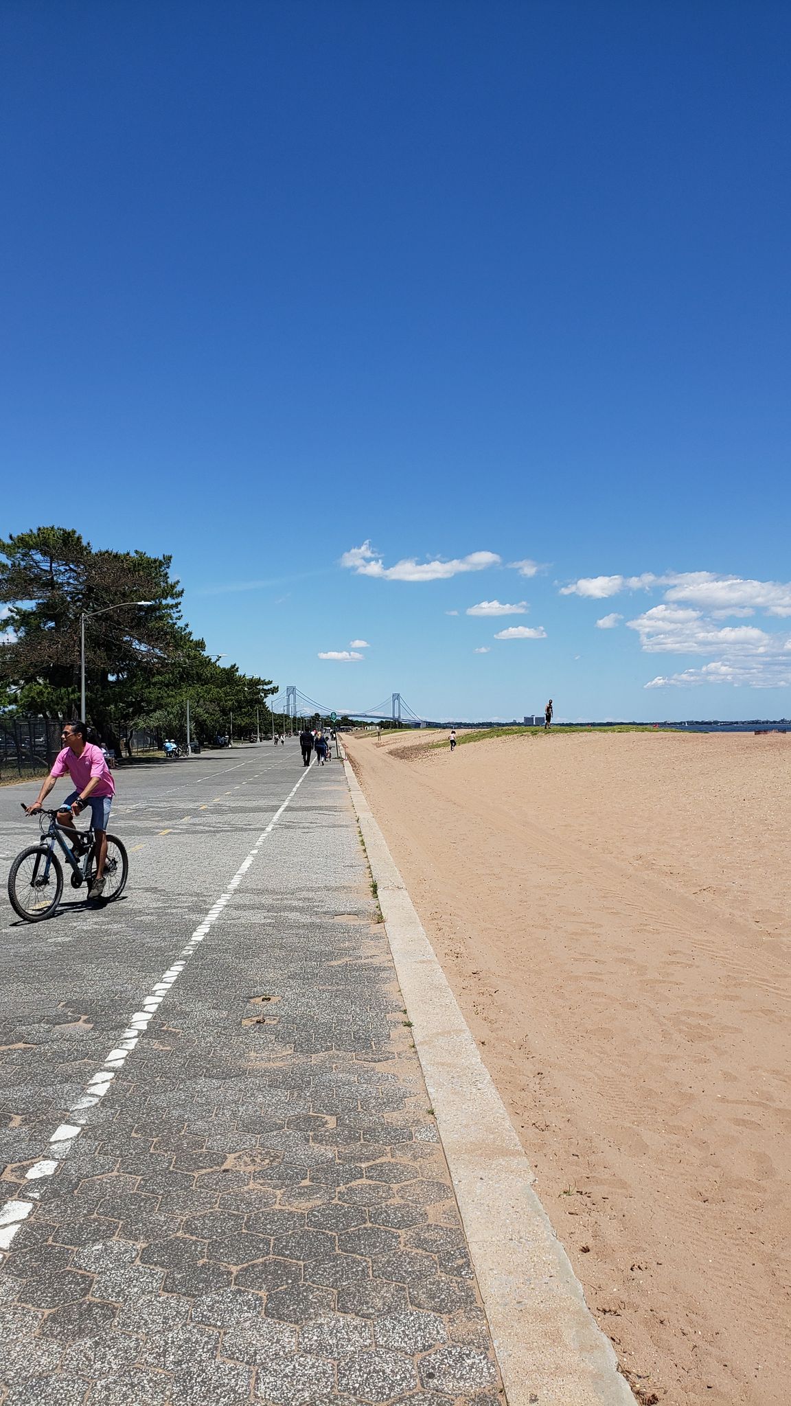 Person cycling on a paved path next to a sandy beach under blue sky. - Fort Wadsworth — Staten Island – Fort Wadsworth loop from Clifton
