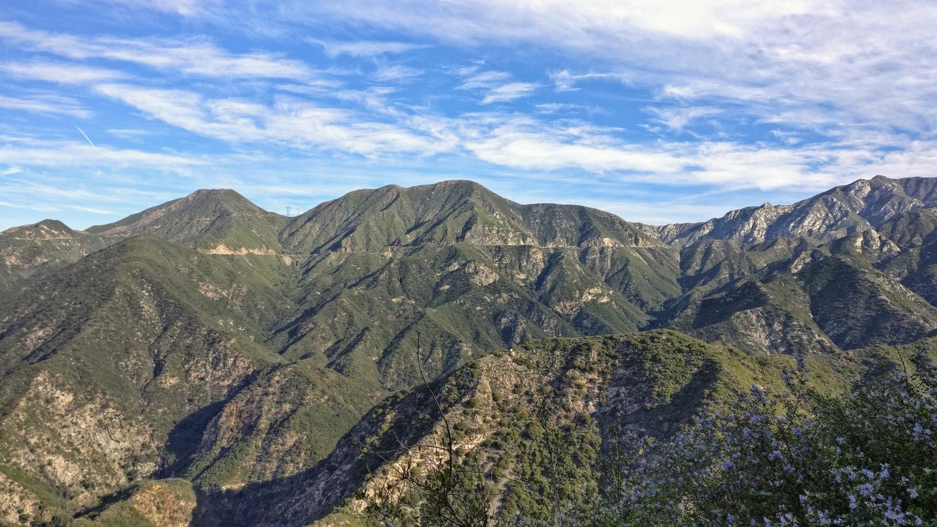 Expansive view of rugged, green mountains under a bright, cloudy blue sky.