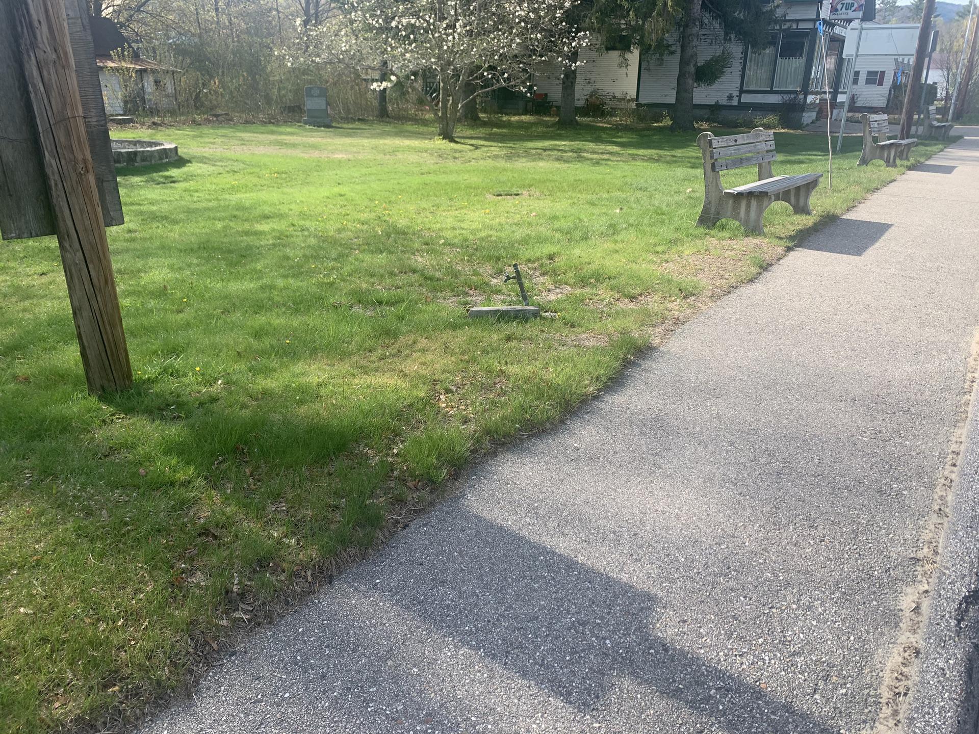 A park bench next to a sidewalk and grassy area on a sunny day.