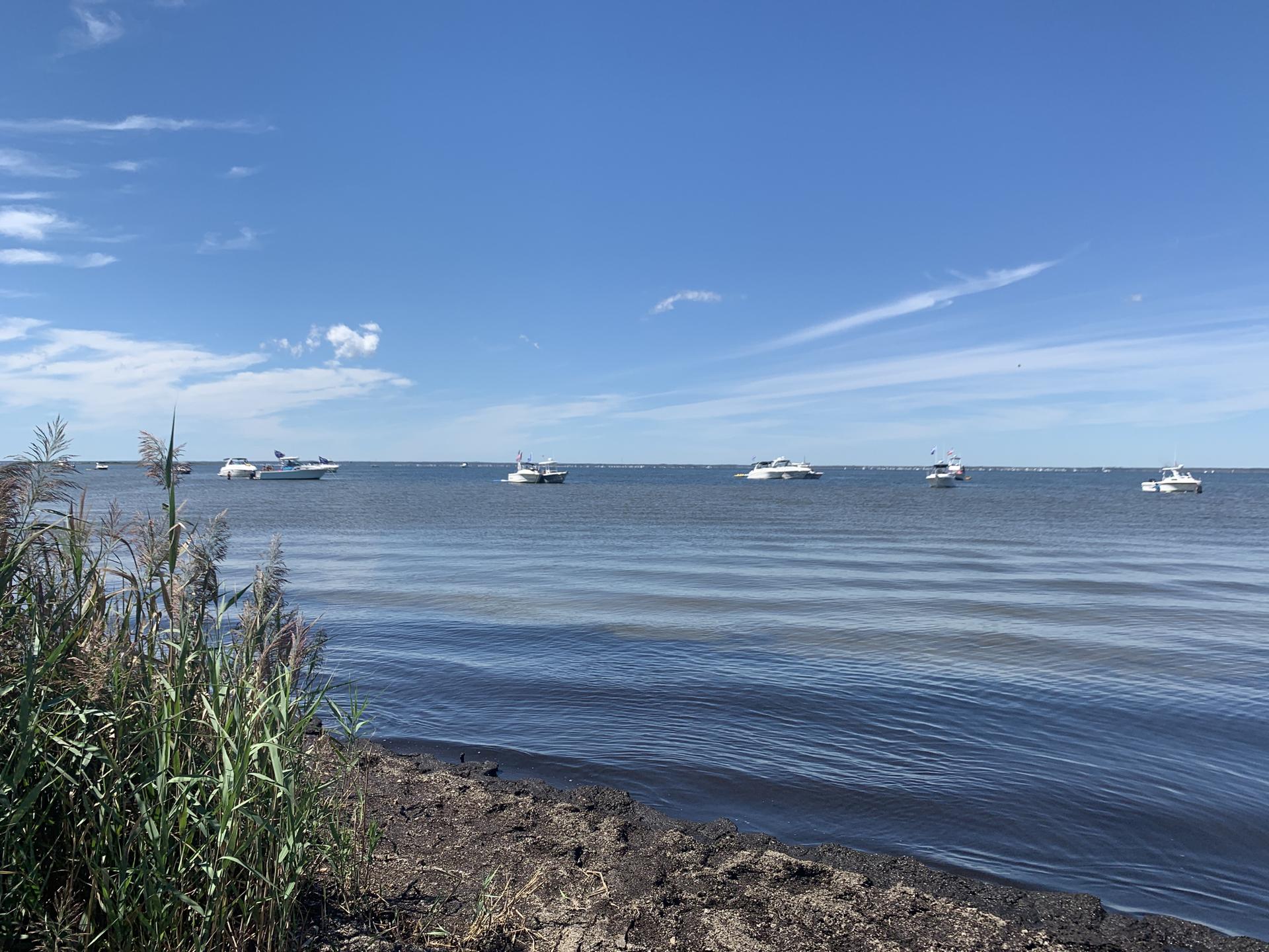 Several boats are anchored on calm water under a bright blue sky with clouds.