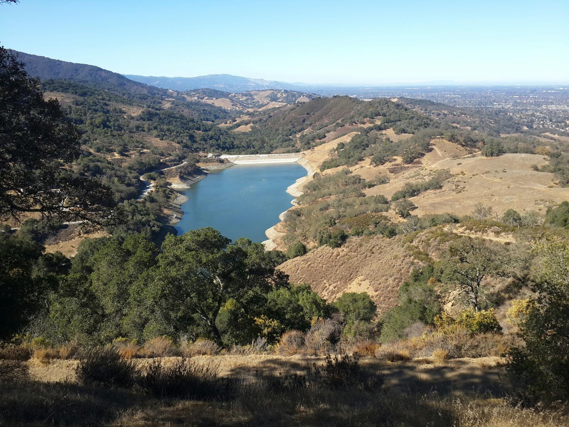 Sunny aerial view of a blue lake nestled among green and dry hills.