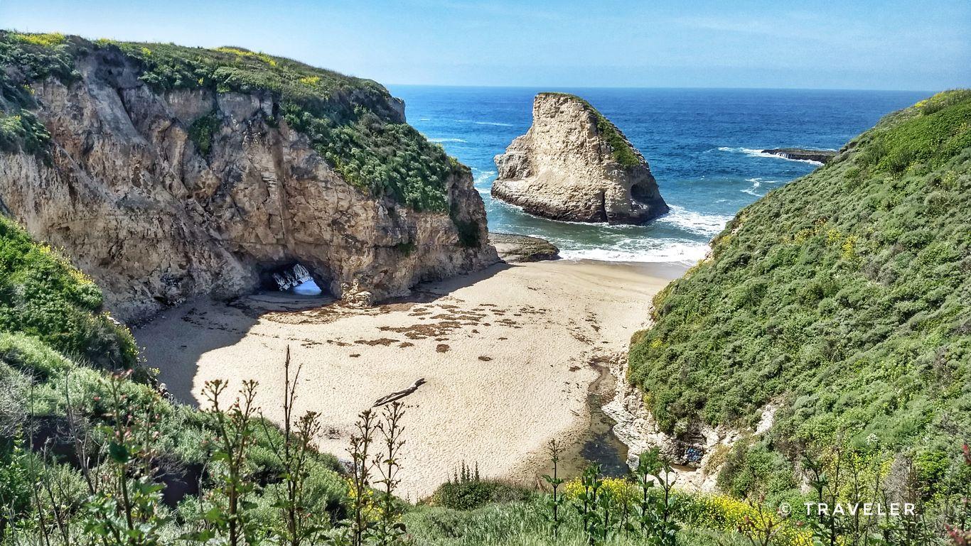 Sandy beach cove, rocky cliffs, and a sea stack in the bright ocean.