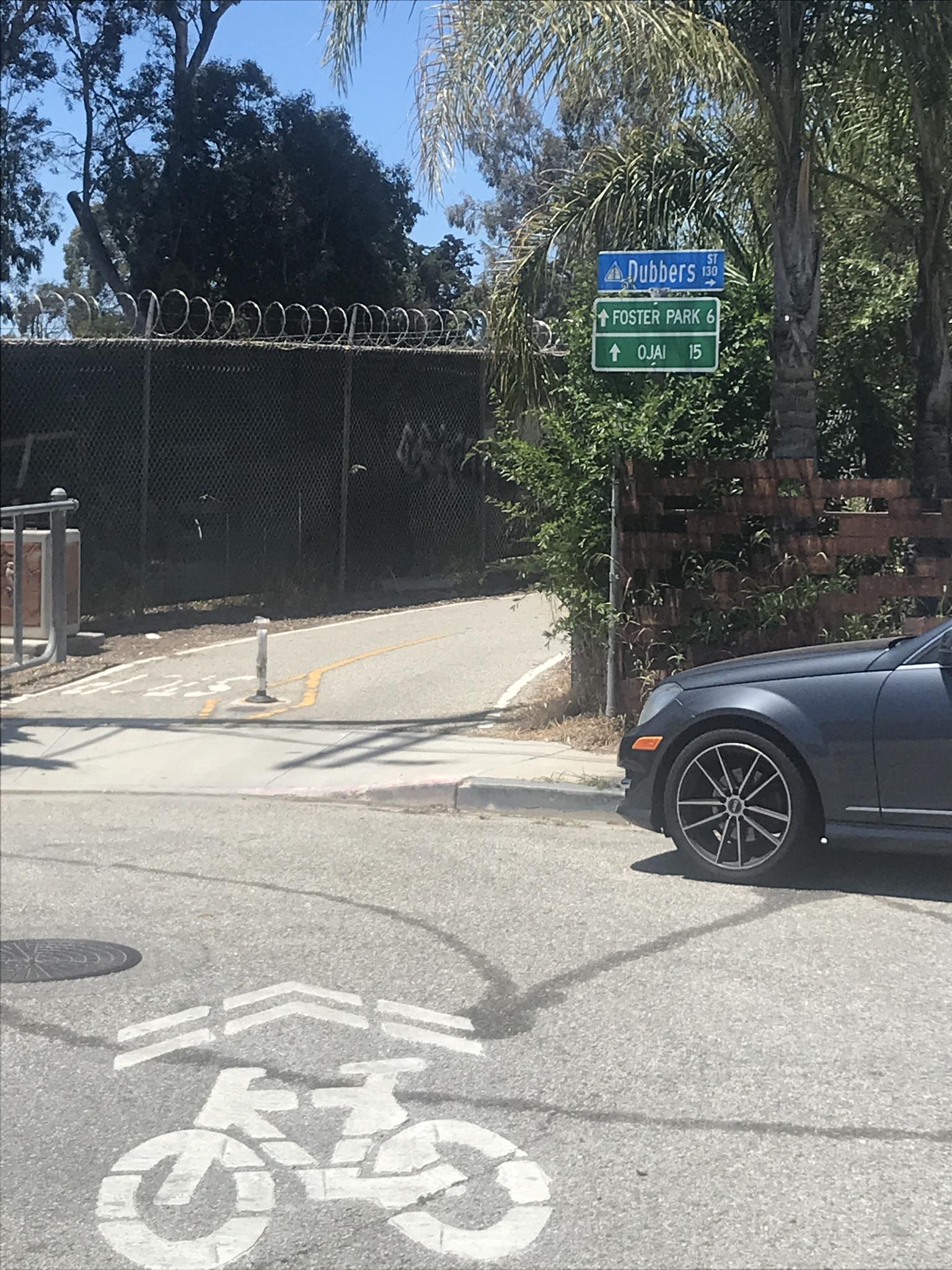 Sunny intersection with road signs, bicycle lane symbol, and parked car.