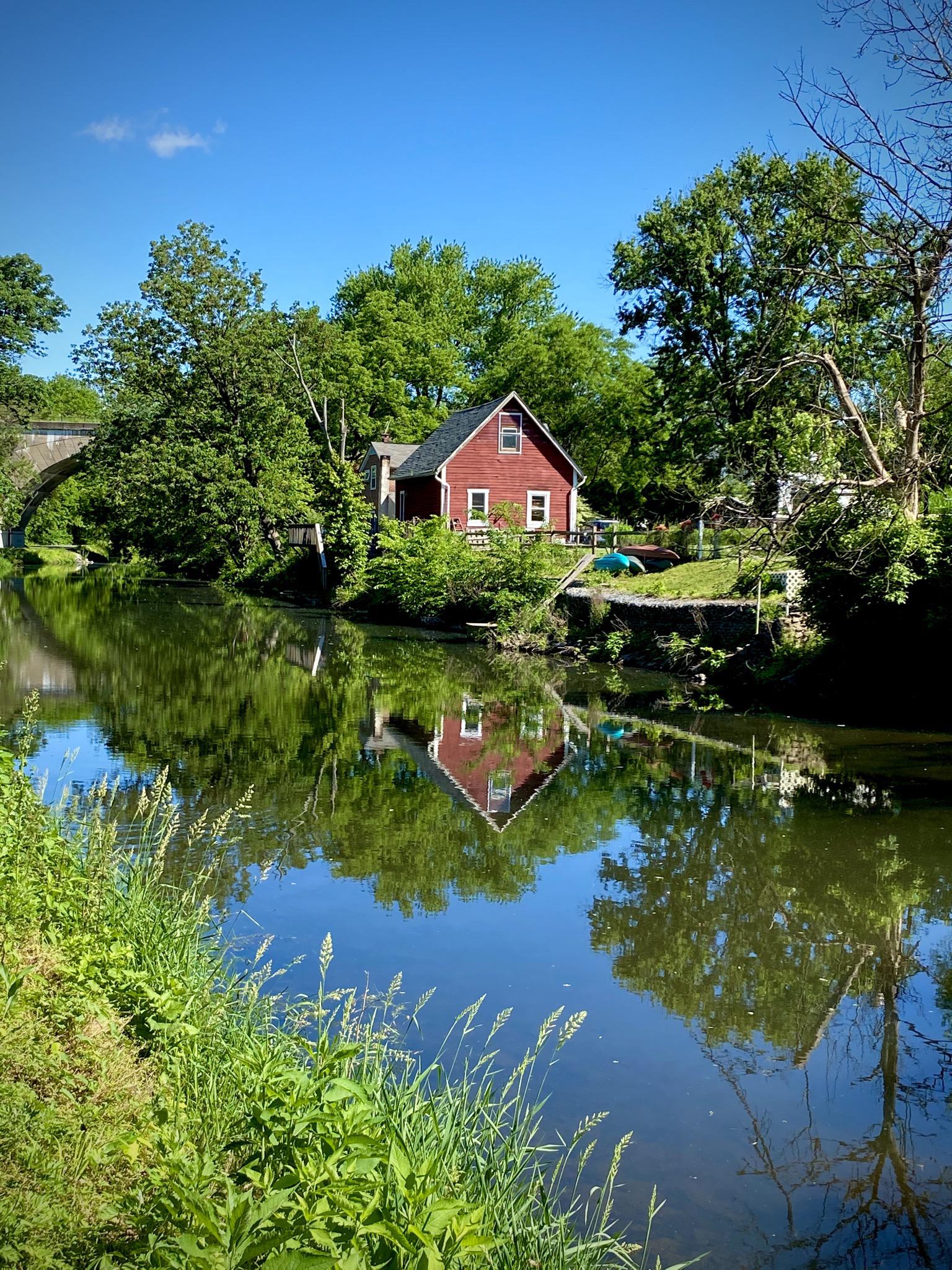 Red house reflected in a calm river, surrounded by lush green trees.
