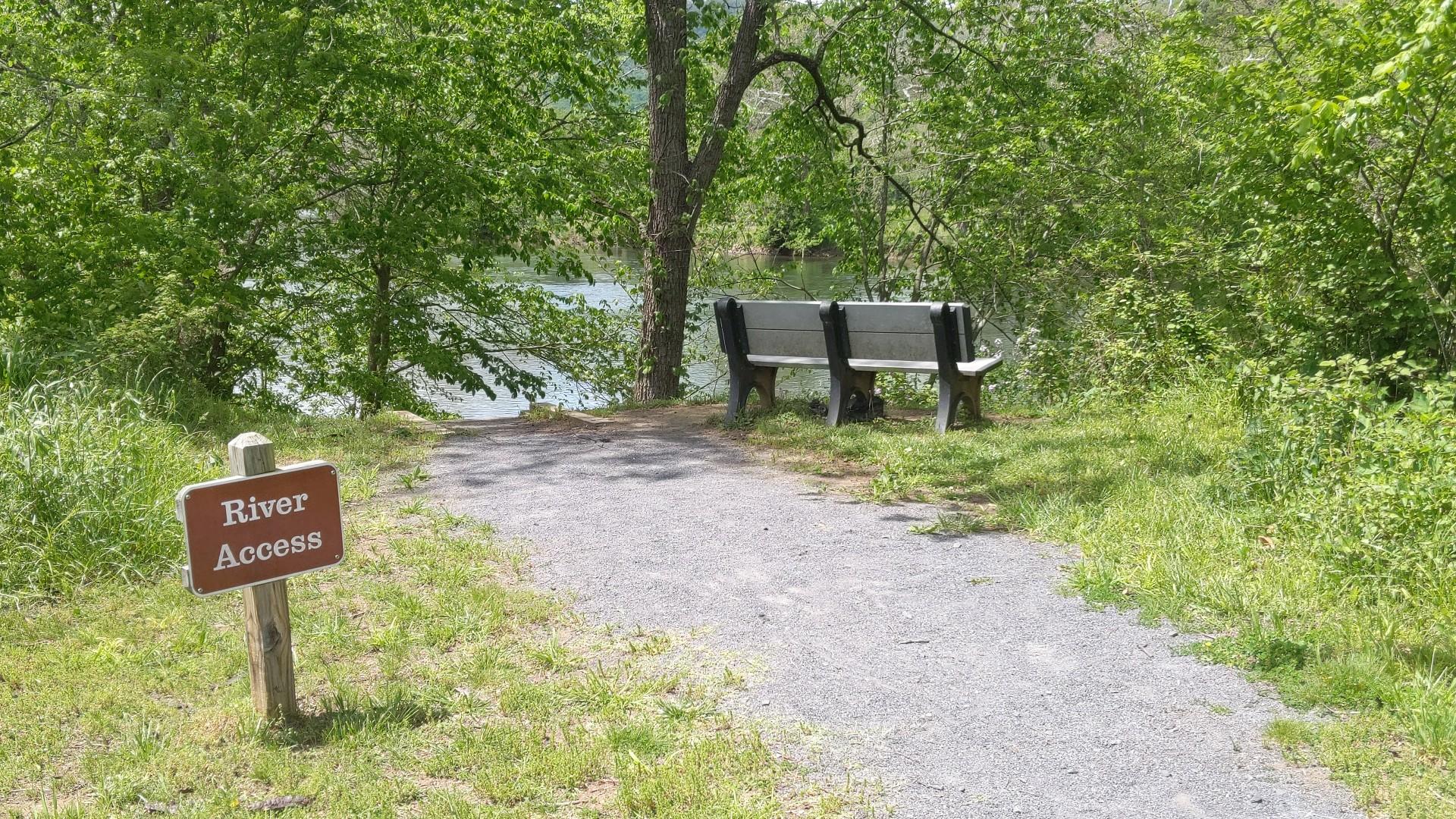 A gravel path leads to a river with a wooden bench.