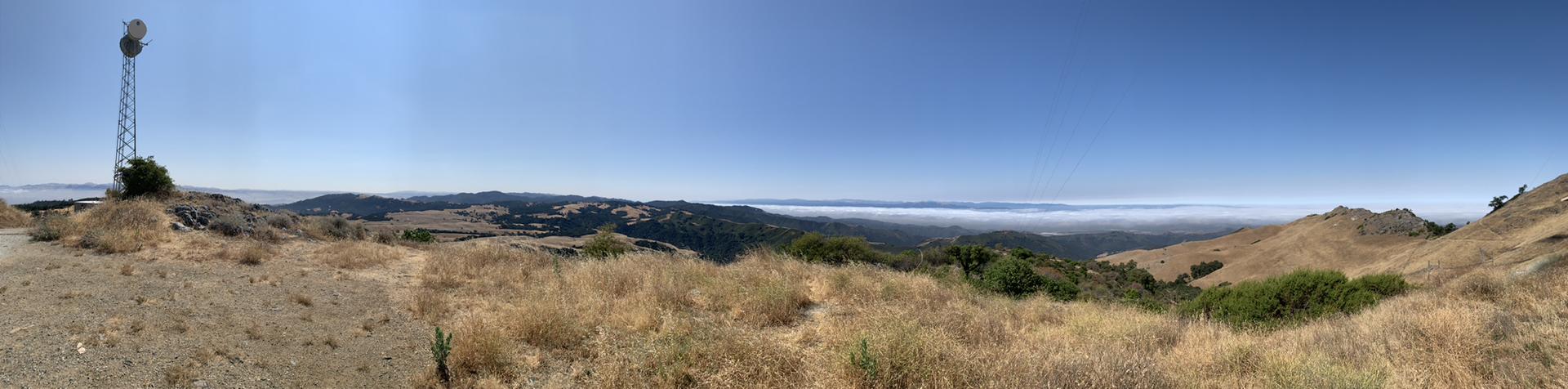 Panoramic view of dry hills, distant fog, and a communication tower under clear sky.