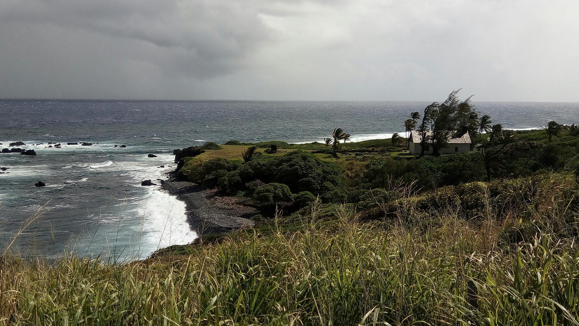 Grassy foreground with a distant coastline, ocean, and stormy sky.