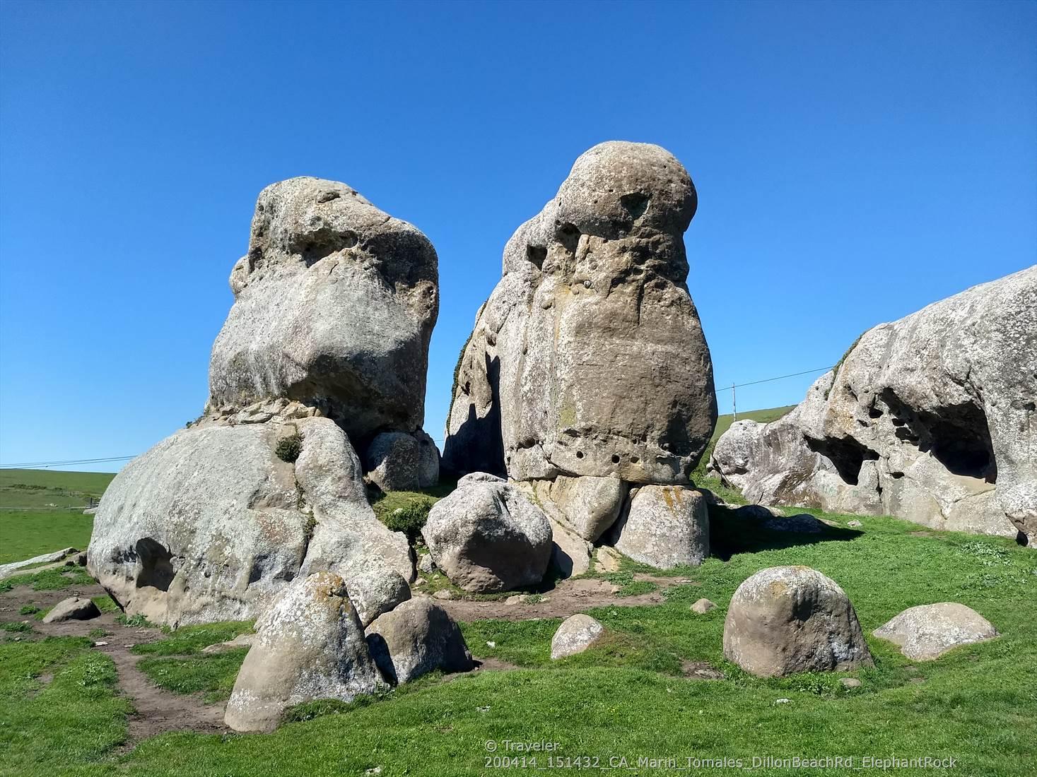 Large, weathered rock formations on a grassy hill under a blue sky.