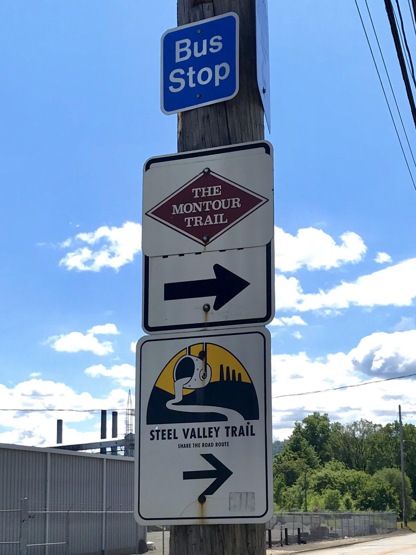 A wooden pole with multiple trail and bus stop signs under a blue sky.