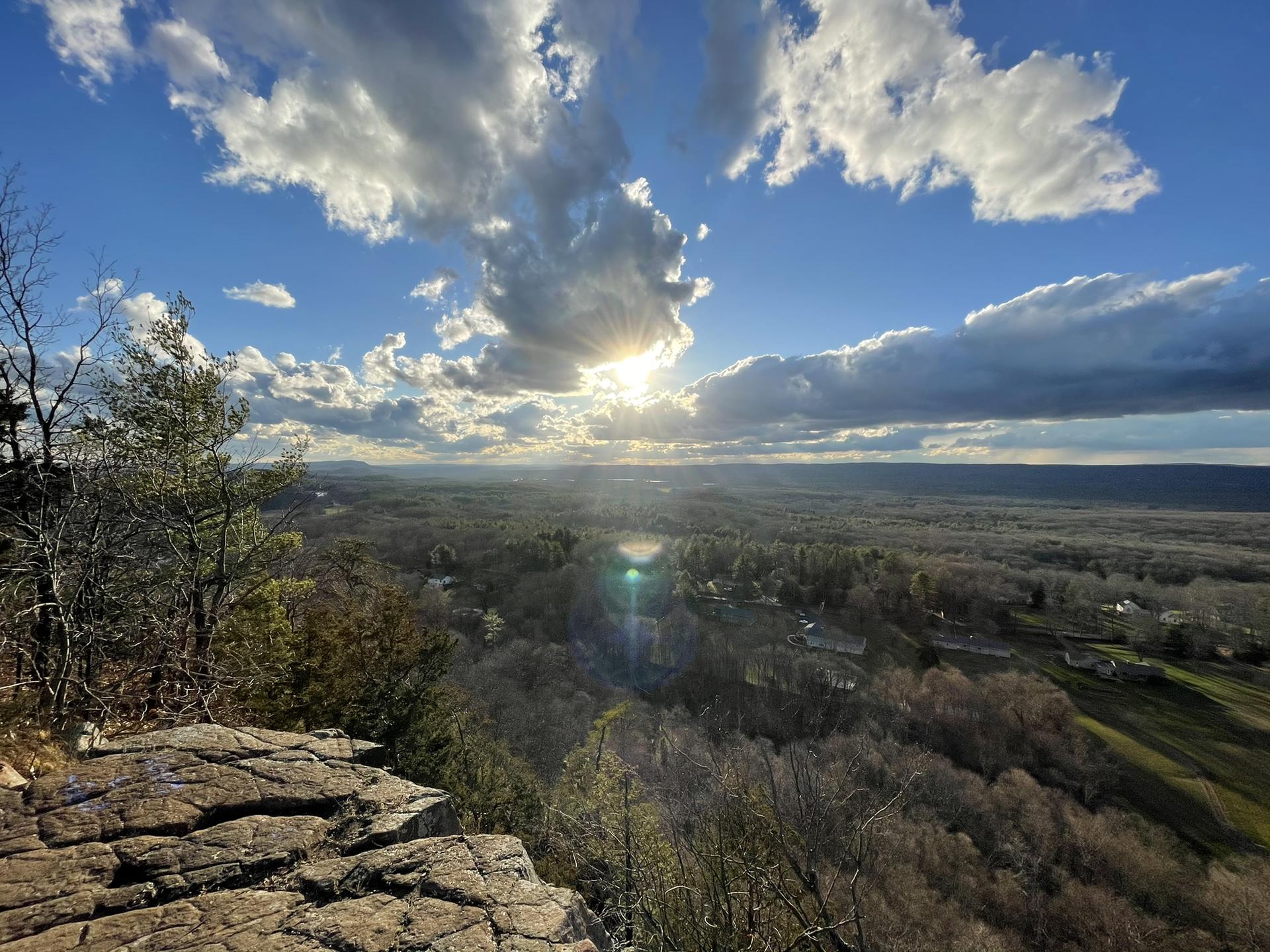 Dramatic sunburst over a vast forested valley from a rocky cliff.