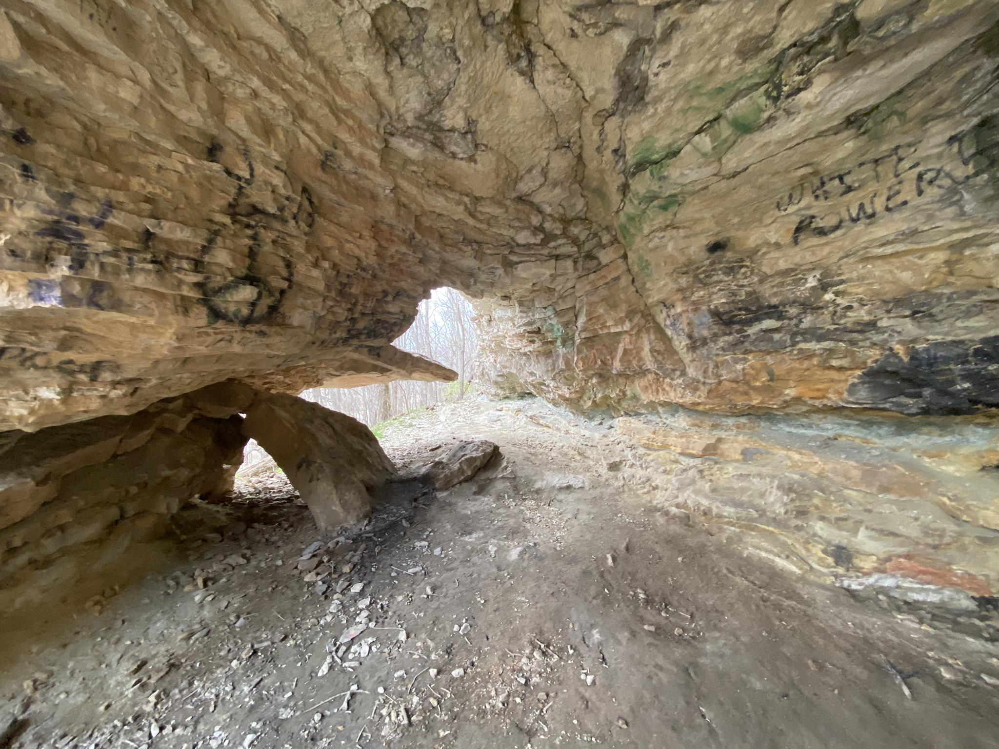 Inside a rocky cave with graffiti, light visible through an opening.