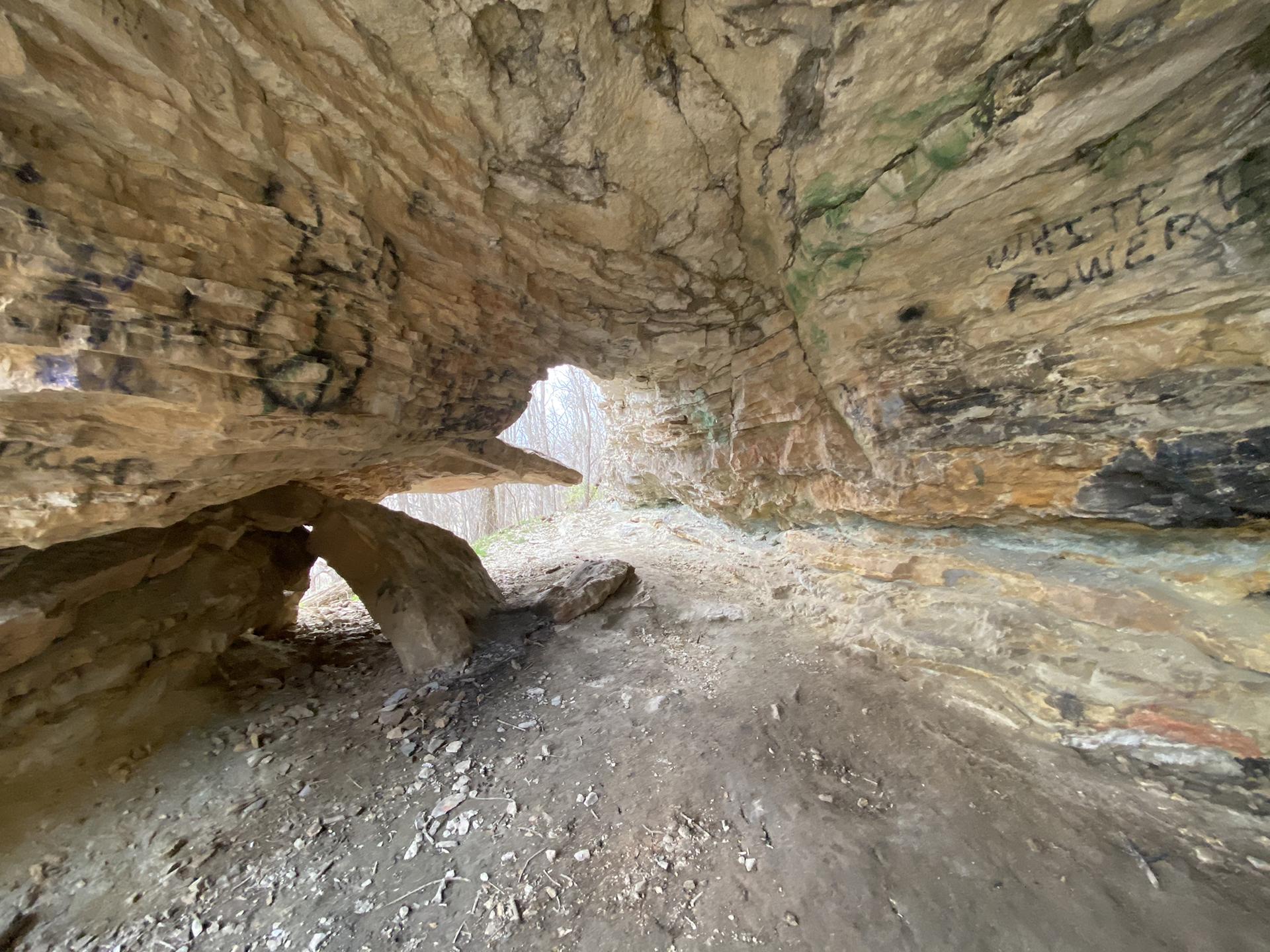 Inside a rocky cave with graffiti, light visible through an opening.