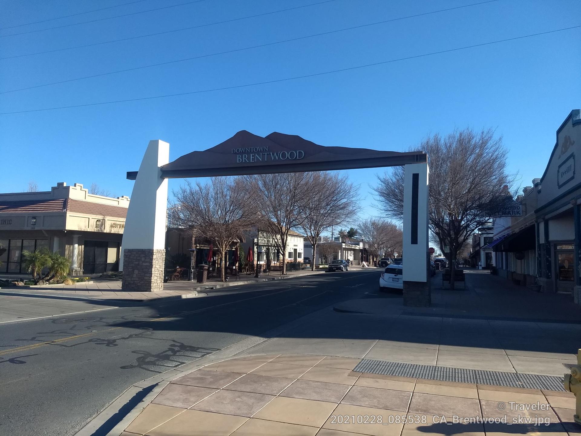 Large archway over a street with buildings and bare trees, sunny.