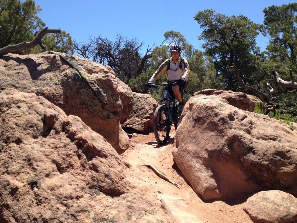 Mountain biker riding through large red rocks on a sunny day.