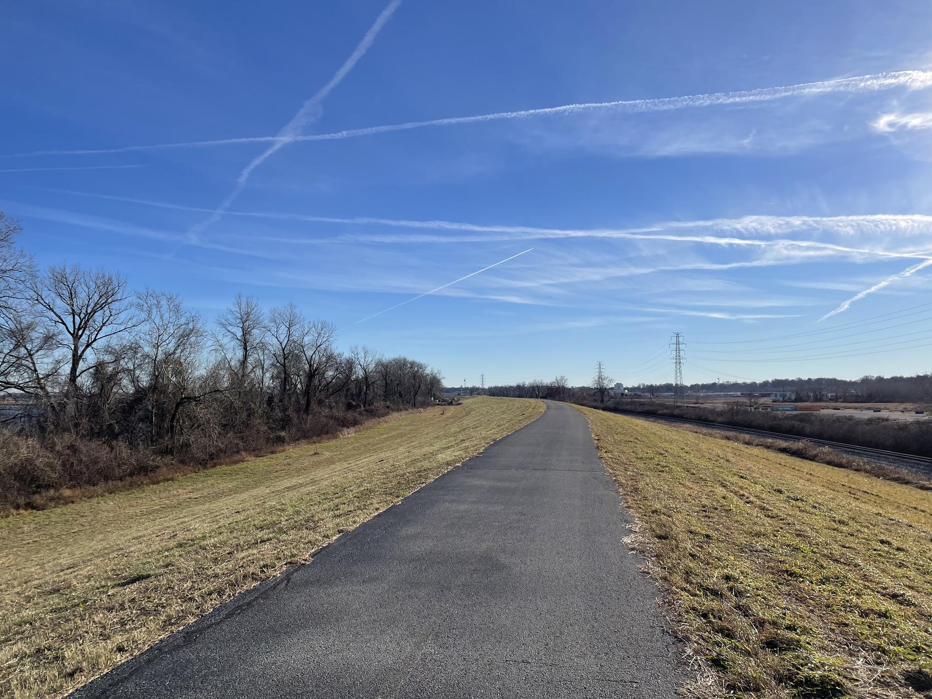 A paved path winds through grassy banks under a clear blue sky.