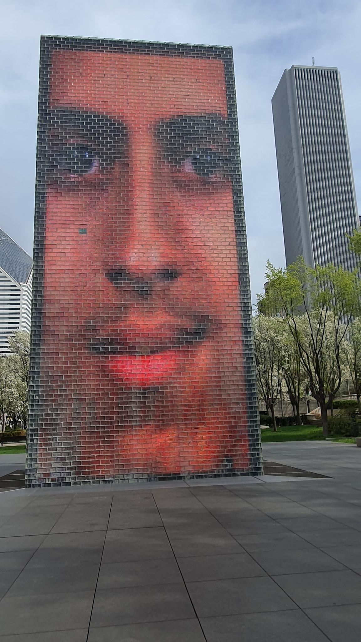 Tall outdoor screen displaying a large human face, with city buildings behind.