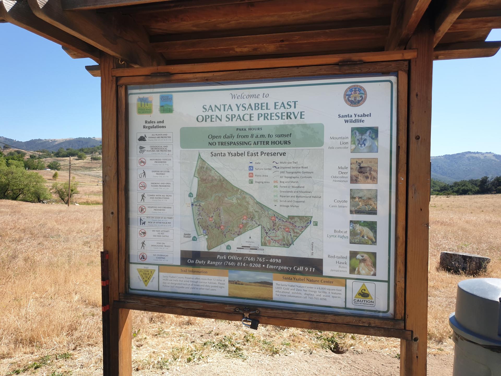 Wooden information kiosk with a map in a dry, sunny field.