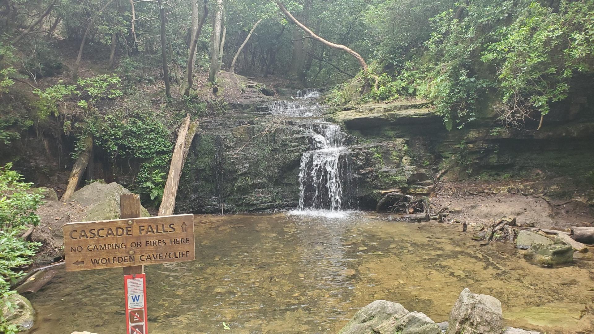 A multi-tiered waterfall cascades into a clear pool surrounded by green forest.