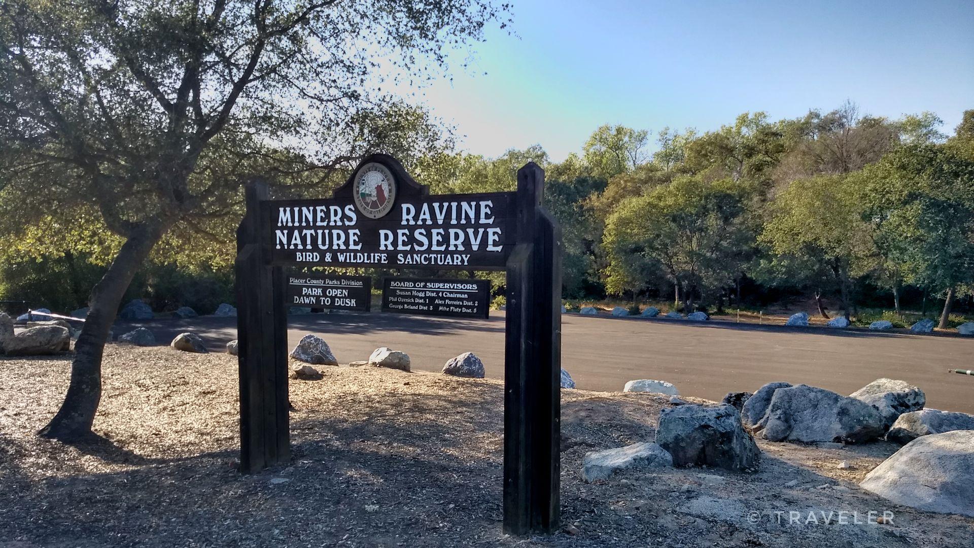 A wooden sign for a nature reserve stands by a paved area.